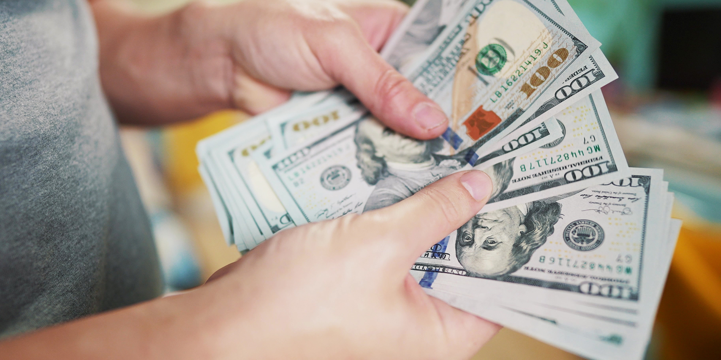Una persona sostiene y cuenta una pila de billetes de 100 dólares | Fuente: Shutterstock