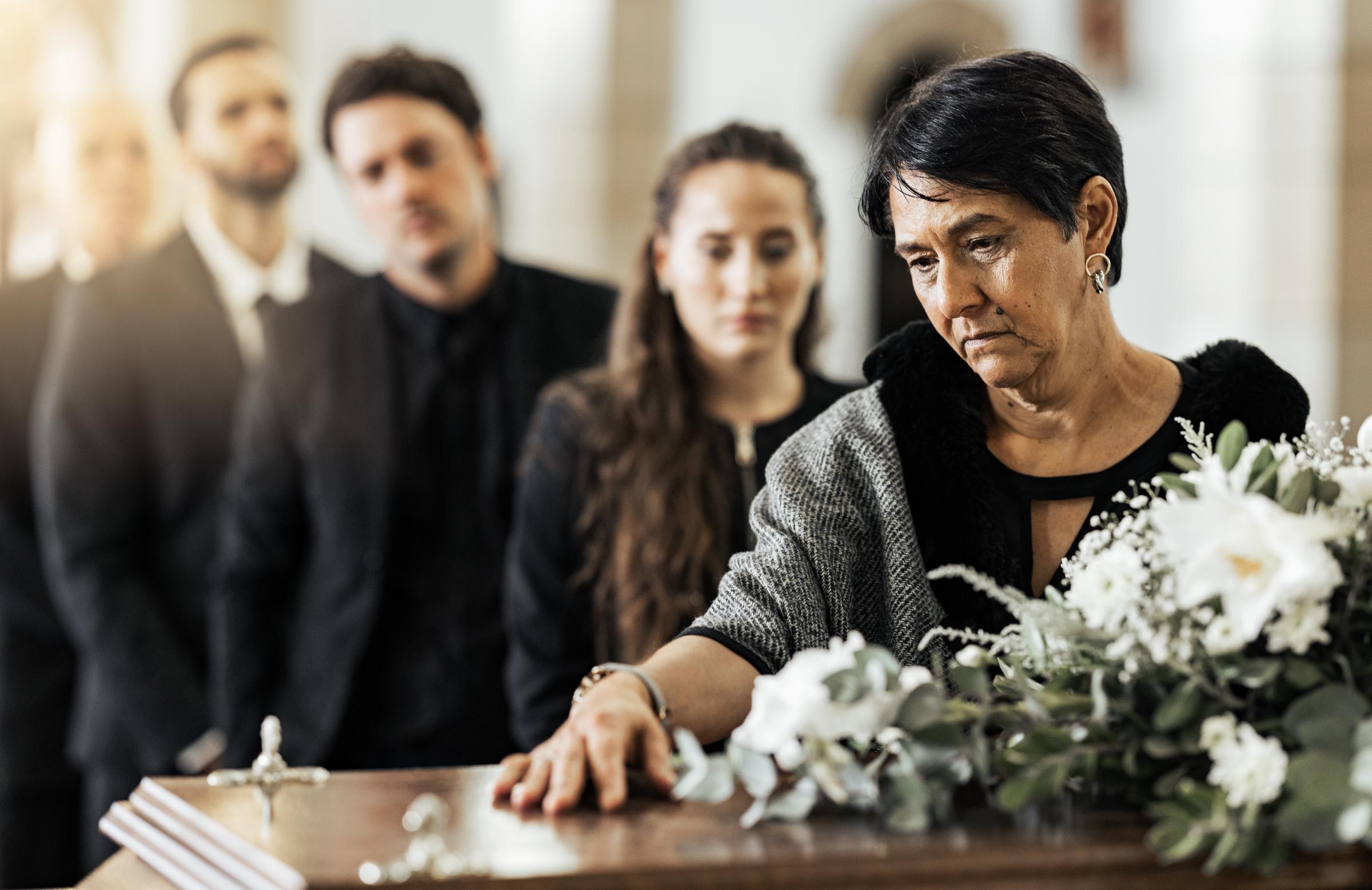 Una mujer coloca su mano sobre el ataúd durante un servicio funerario | Fuente: Shutterstock