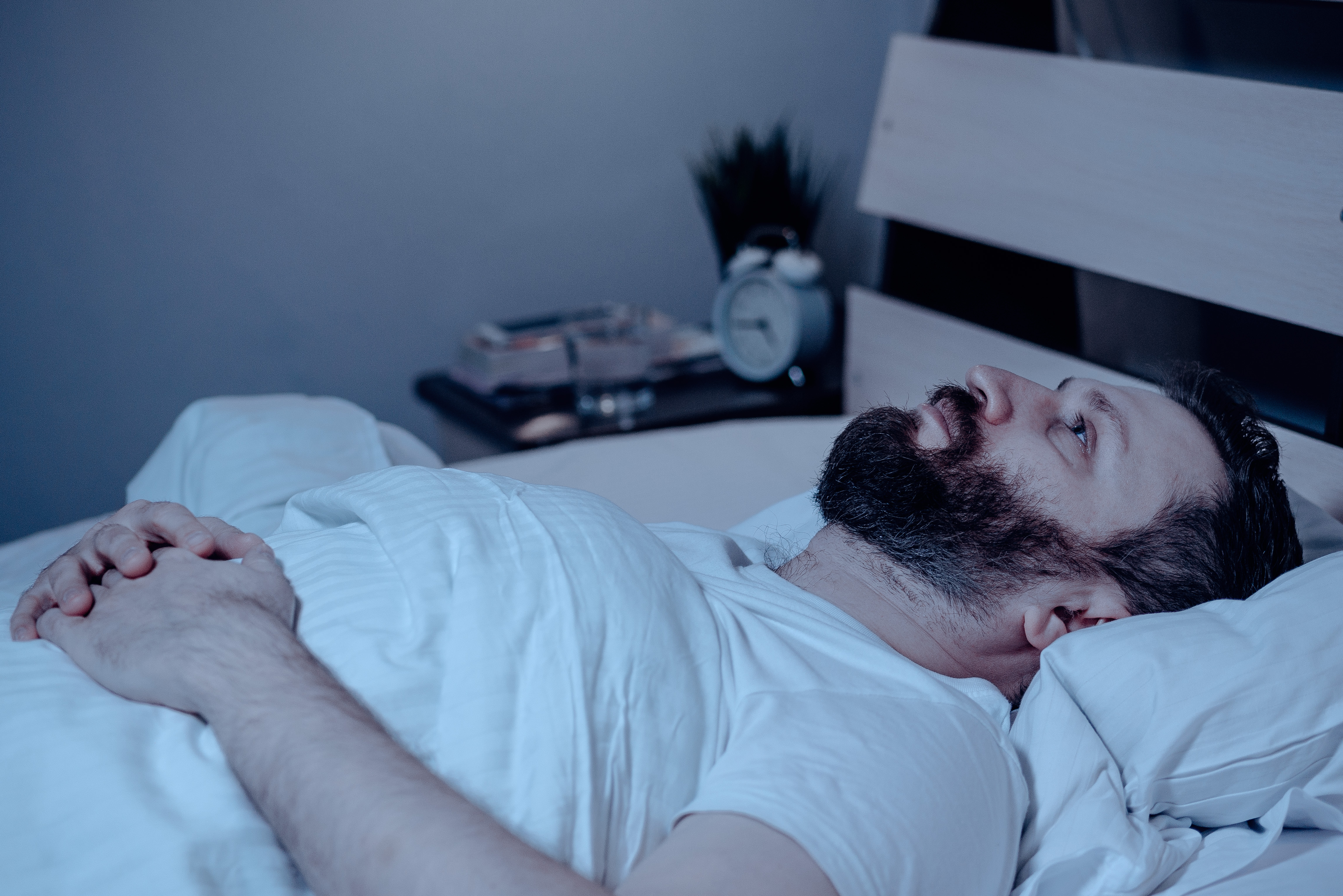 Un hombre barbudo en la cama por la noche no puede dormir, es infeliz y está muy cansado. | Fuente: Shutterstock
