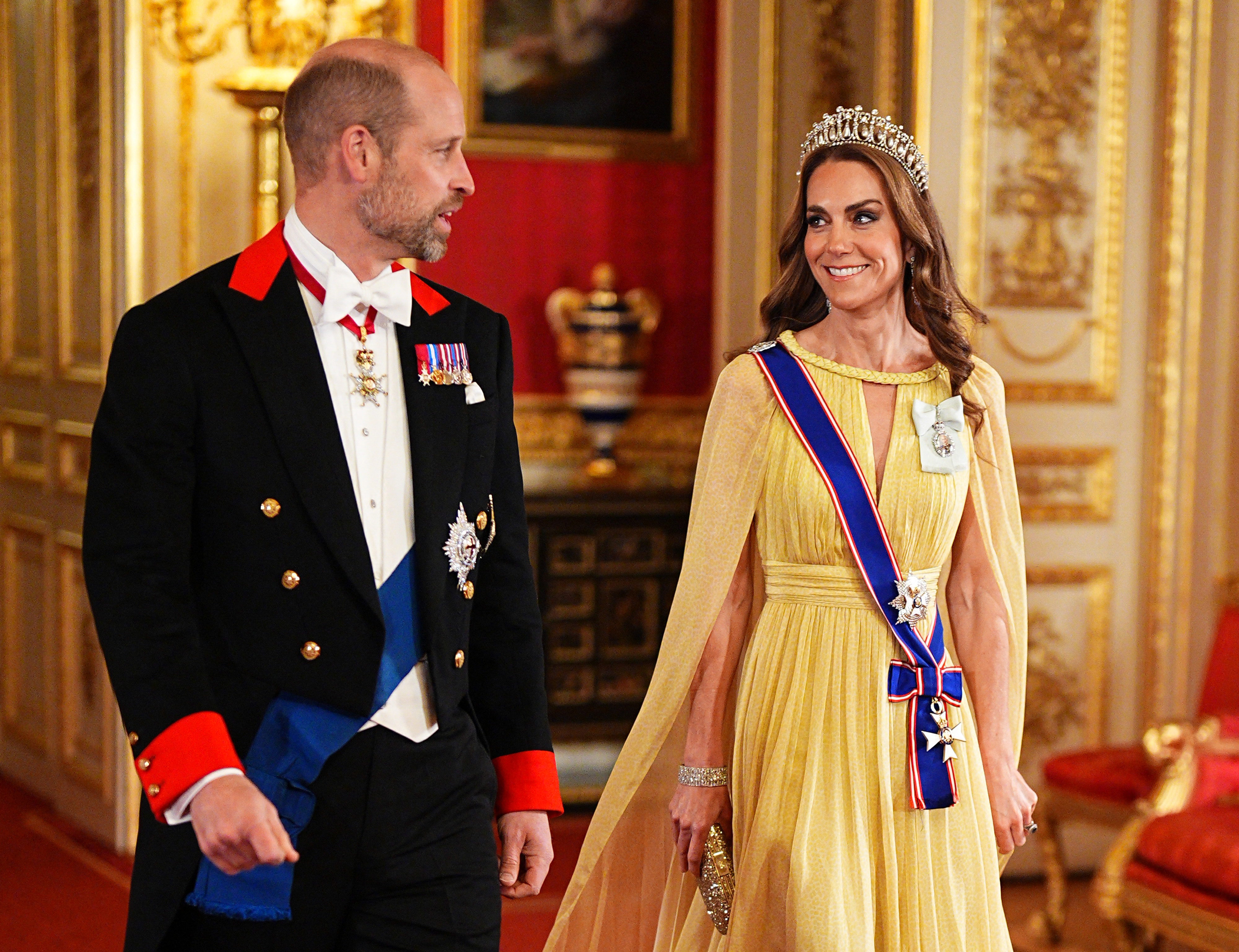 Catherine, princesa de Gales, intercambia una alegre sonrisa con el príncipe William mientras recorren los salones del castillo de Windsor el 20 de octubre de 2026. Con la tiara Lover's Knot de la reina Mary, Catherine deslumbra con un vestido amarillo intenso con capa de Elie Saab, la banda de la Real Orden Victoriana y la Orden de la Familia Real del rey Charles III. William la acompaña con frac formal de Windsor y la banda de la Orden de la Jarretera. | Fuente: Getty Images