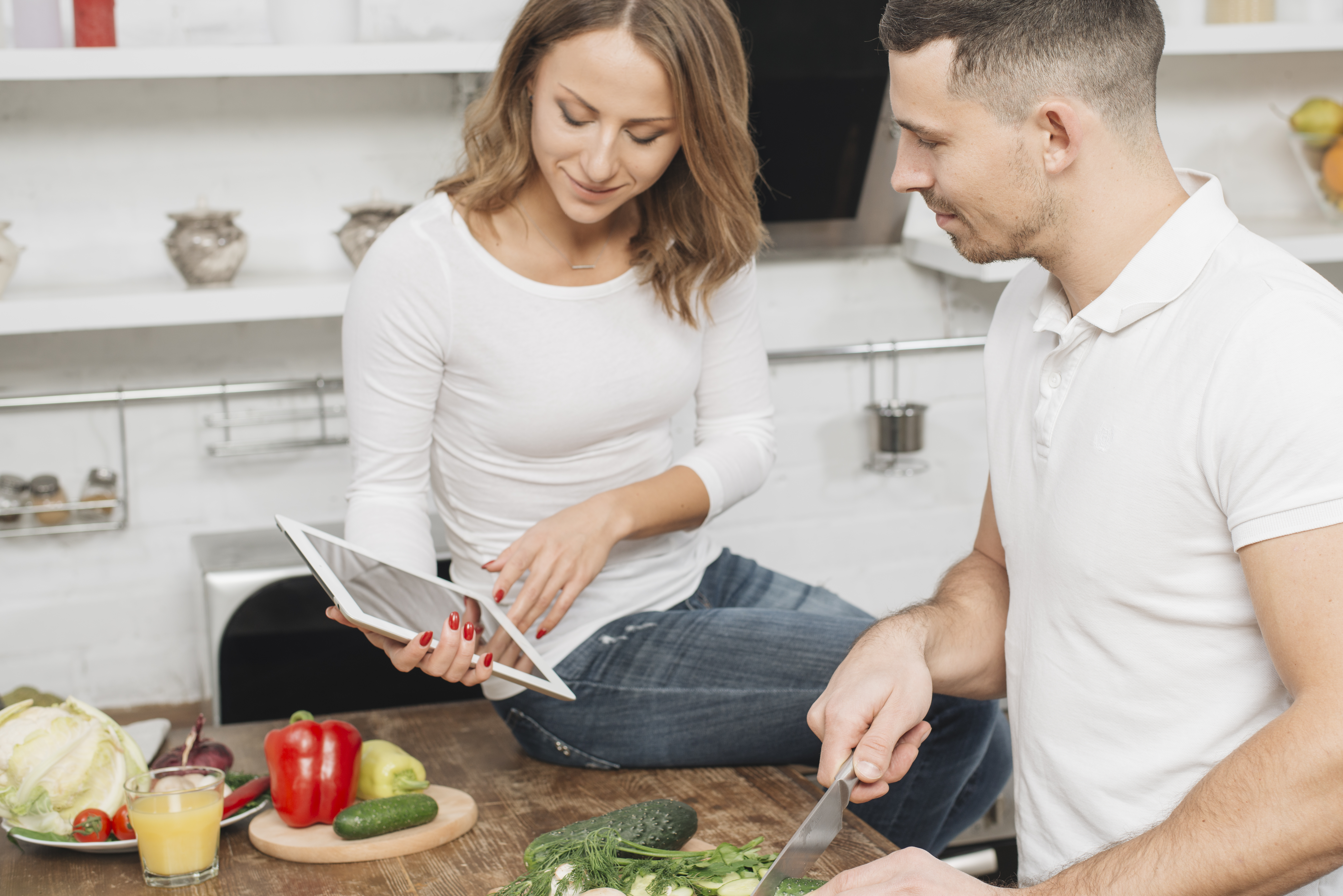 Mujer mostrando una tablet a un hombre mientras cocina en la cocina | Fuente: Freepik