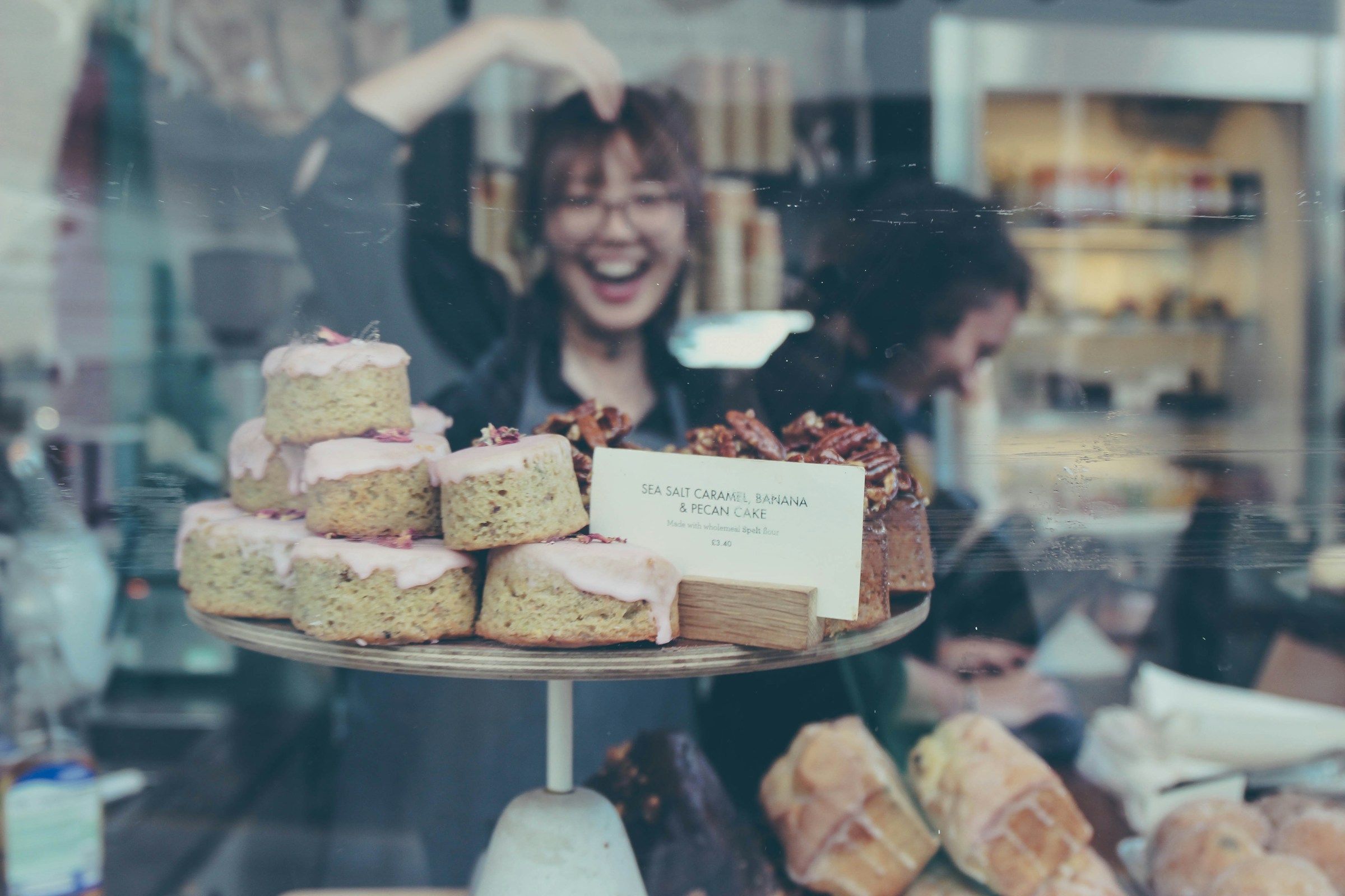 El reflejo de una joven sonriente en el cristal del expositor de una panadería | Fuente: Unsplash