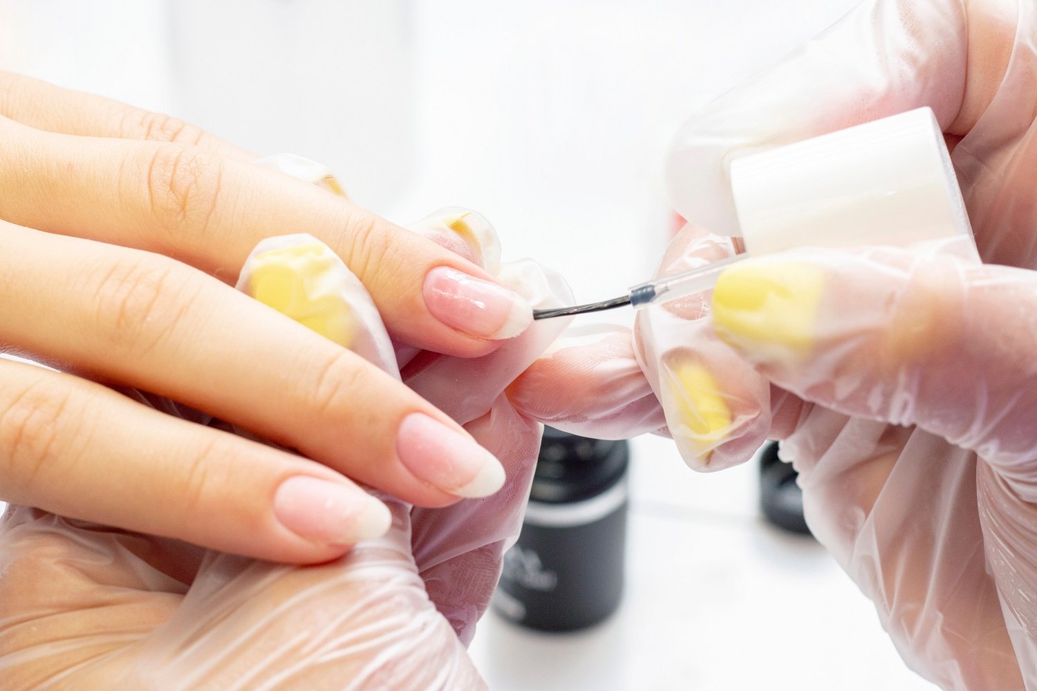 Profesional manicurista aplicando esmalte base a las uñas de una mujer. | Foto: Shutterstock