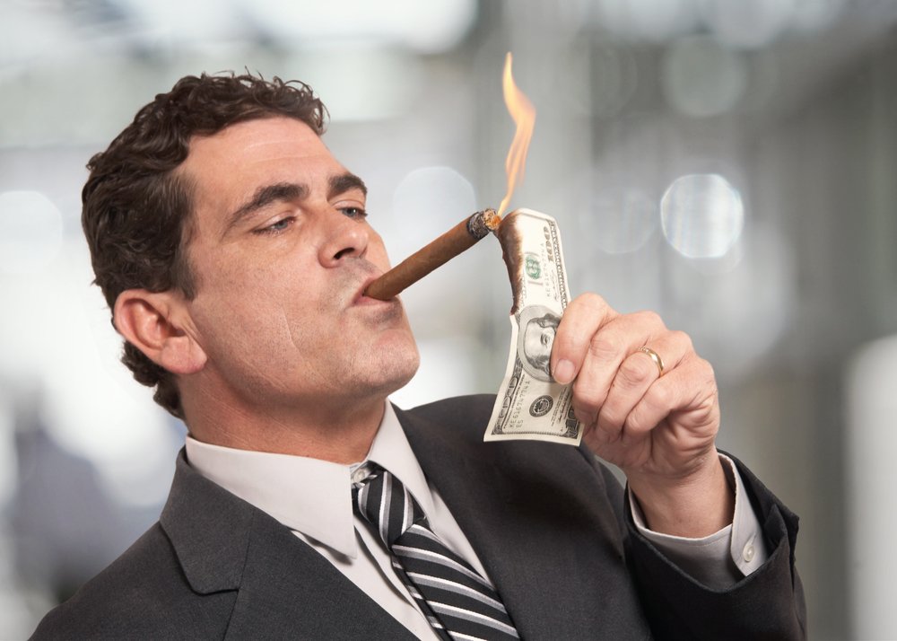 Rico hombre de negocios encendiendo cigarros con un billete de $100. | Fuente: Shutterstock