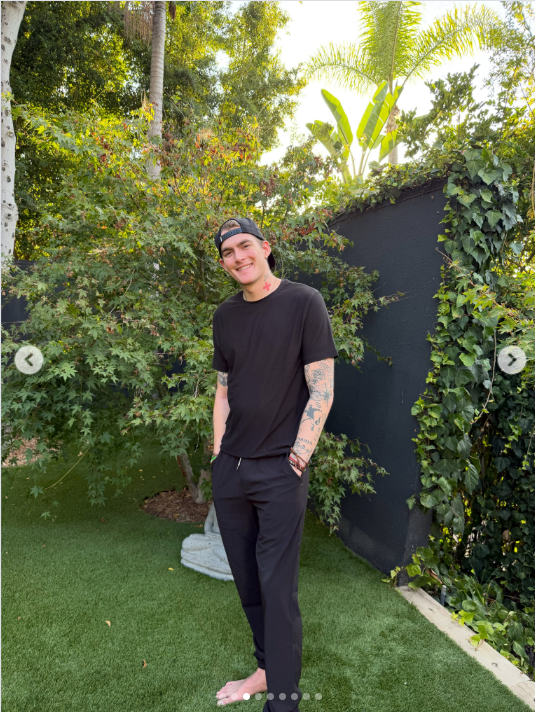 Presley Gerber inclina la cabeza y sonríe ampliamente a la cámara, posando descalzo y con las manos en los bolsillos mientras posa entre la exuberante vegetación. | Fuente: Instagram/presleygerber
