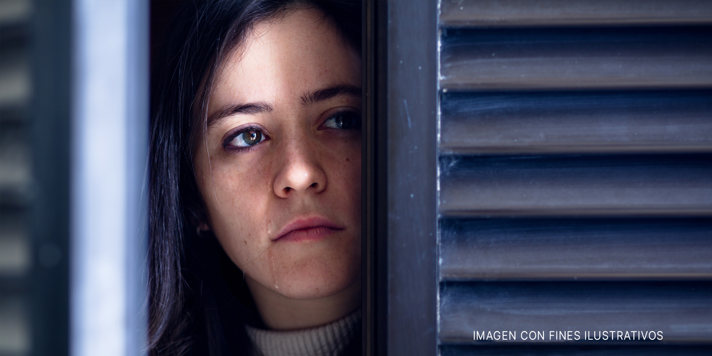 Mujer mirando a través de una puerta/ventana y llorando | Foto: Shutterstock