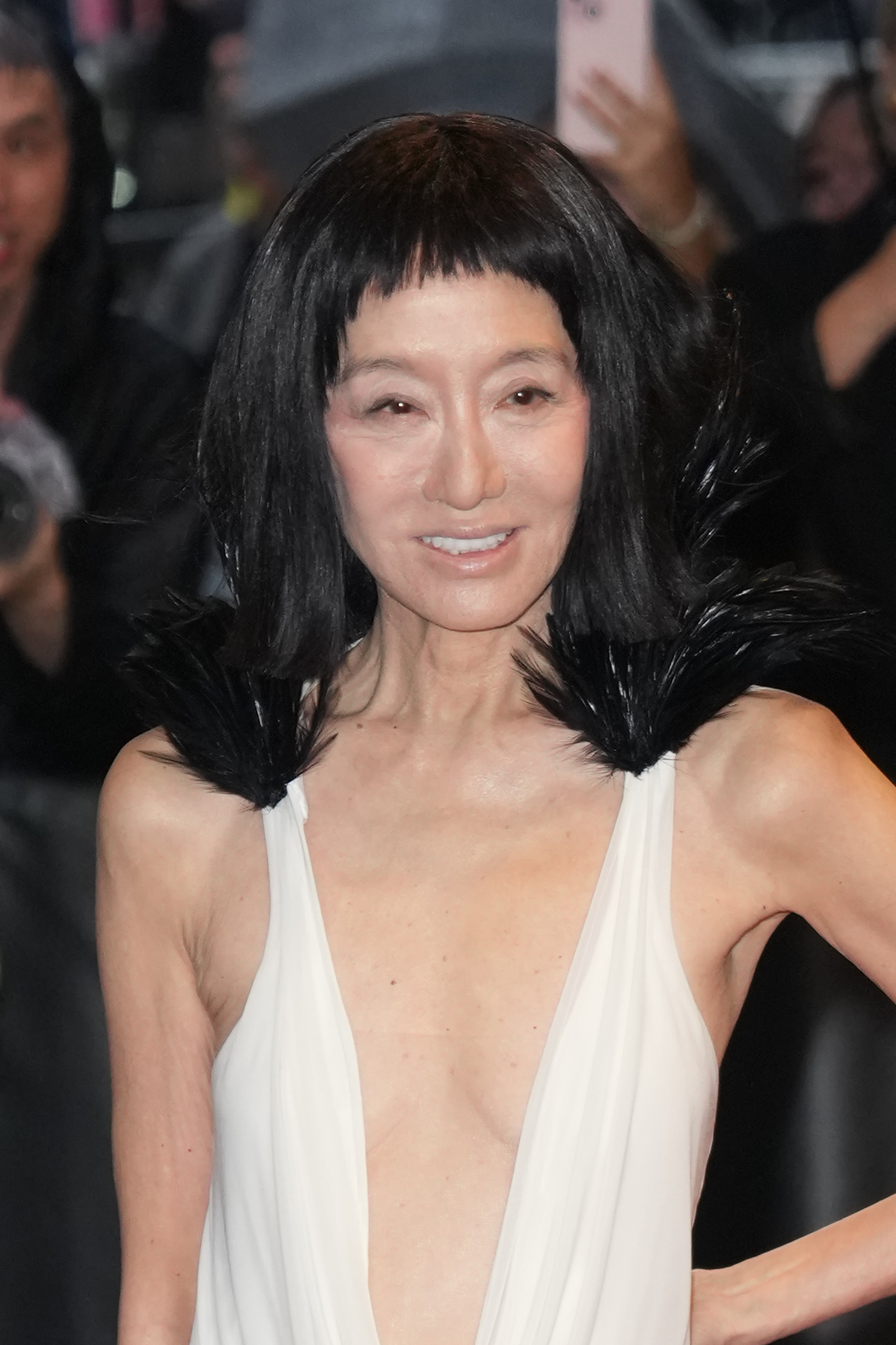 Vera Wang sonríe a las cámaras con un vestido marfil de gran caída con espectaculares detalles de plumas, revelando un lado más suave de su atrevido conjunto para la alfombra roja.