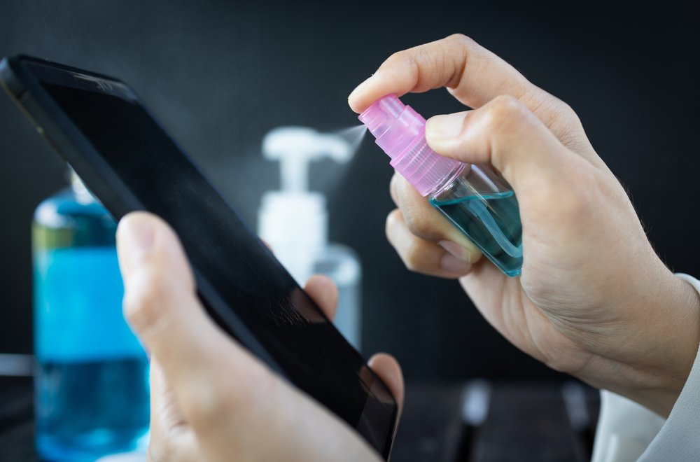 Mujer rocía desinfectante en spray en el teléfono móvil para prevenir la infección del virus Covid-19. | Foto: Shutterstock