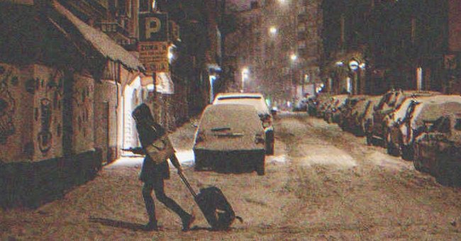 Mujer cruzando la calle de noche con una maleta | Foto: Shutterstock