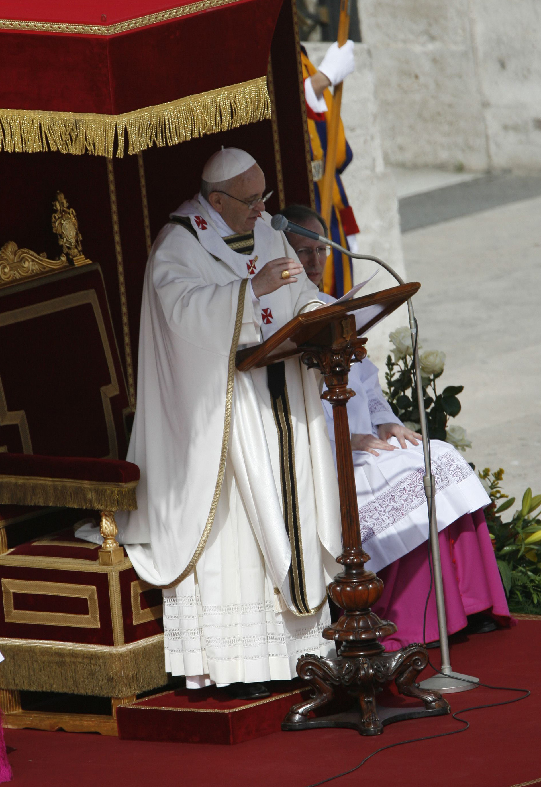 El papa Francisco pronuncia un sermón desde un atril de madera tallada, ataviado con vestiduras de color crema con cruces rojas, junto a una silla con forma de trono y adornos dorados.