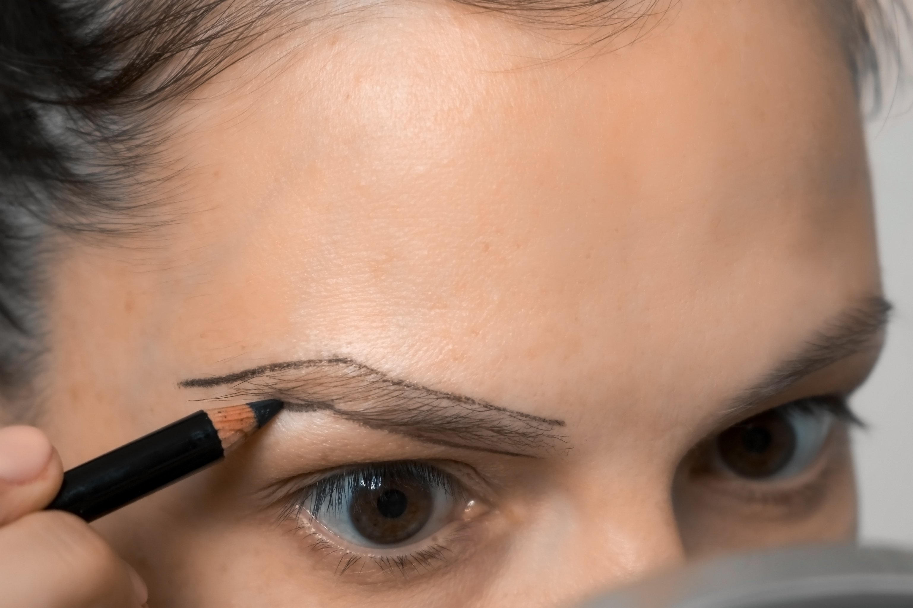 Mujer dibujando el contorno de las cejas usando lápiz antes de pintarlas. | Foto: Shutterstock