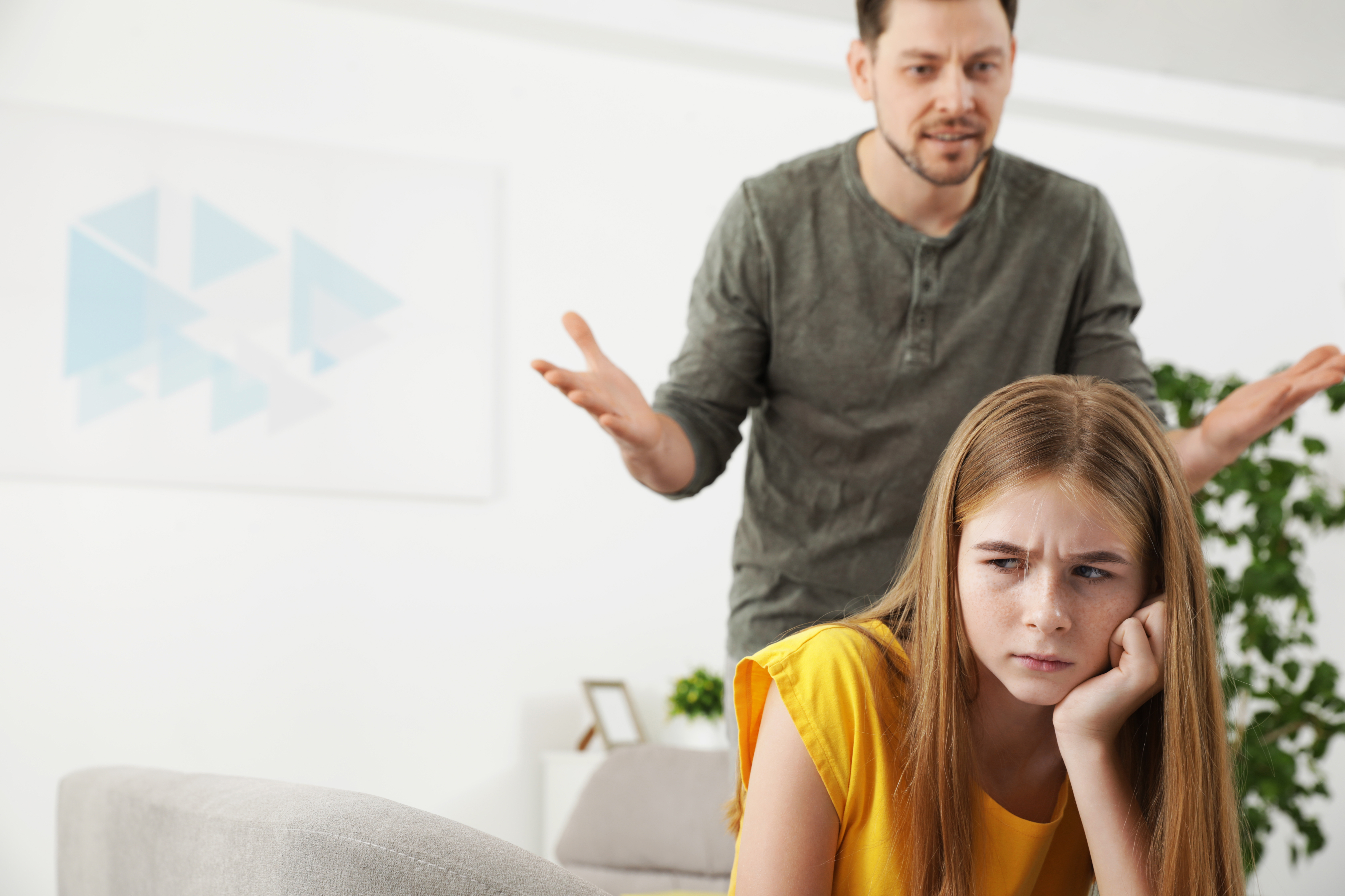 Un hombre enfadado detrás de una chica sentada en un sofá | Foto: Shutterstock