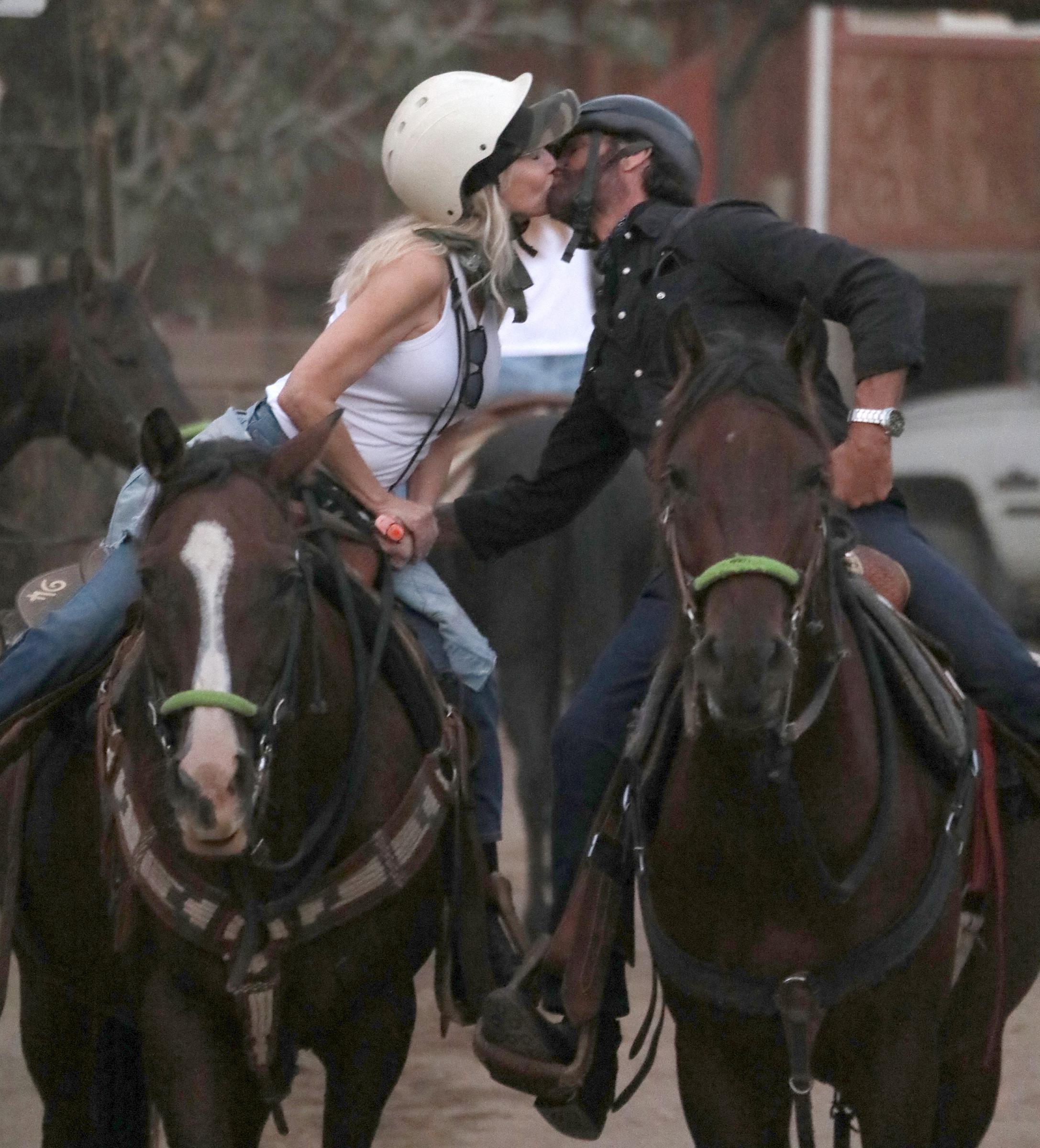 Heather Locklear y Lorenzo Lamas se dan un tierno beso a lomos de sus caballos durante una visita al Sunset Ranch, en las colinas de Hollywood, el 22 de septiembre de 2026, en Los Ángeles, California. Vestidos para montar a caballo con cascos protectores y jeans, Locklear lleva una camiseta sin mangas blanca mientras se inclina para besar a Lamas, que luce una camisa negra abotonada y un reloj de pulsera. | Fuente: Getty Images