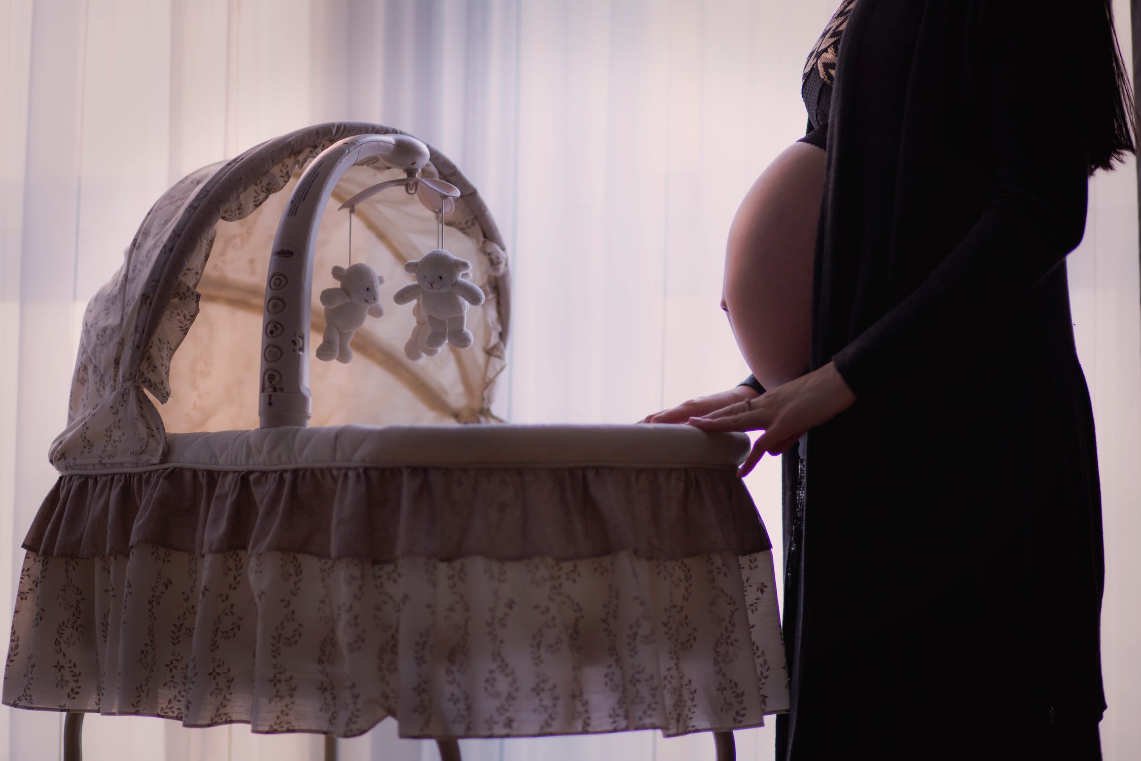 Mujer junto a una pequeña cuna mostrando su panza de embarazada. | Foto: Unsplash