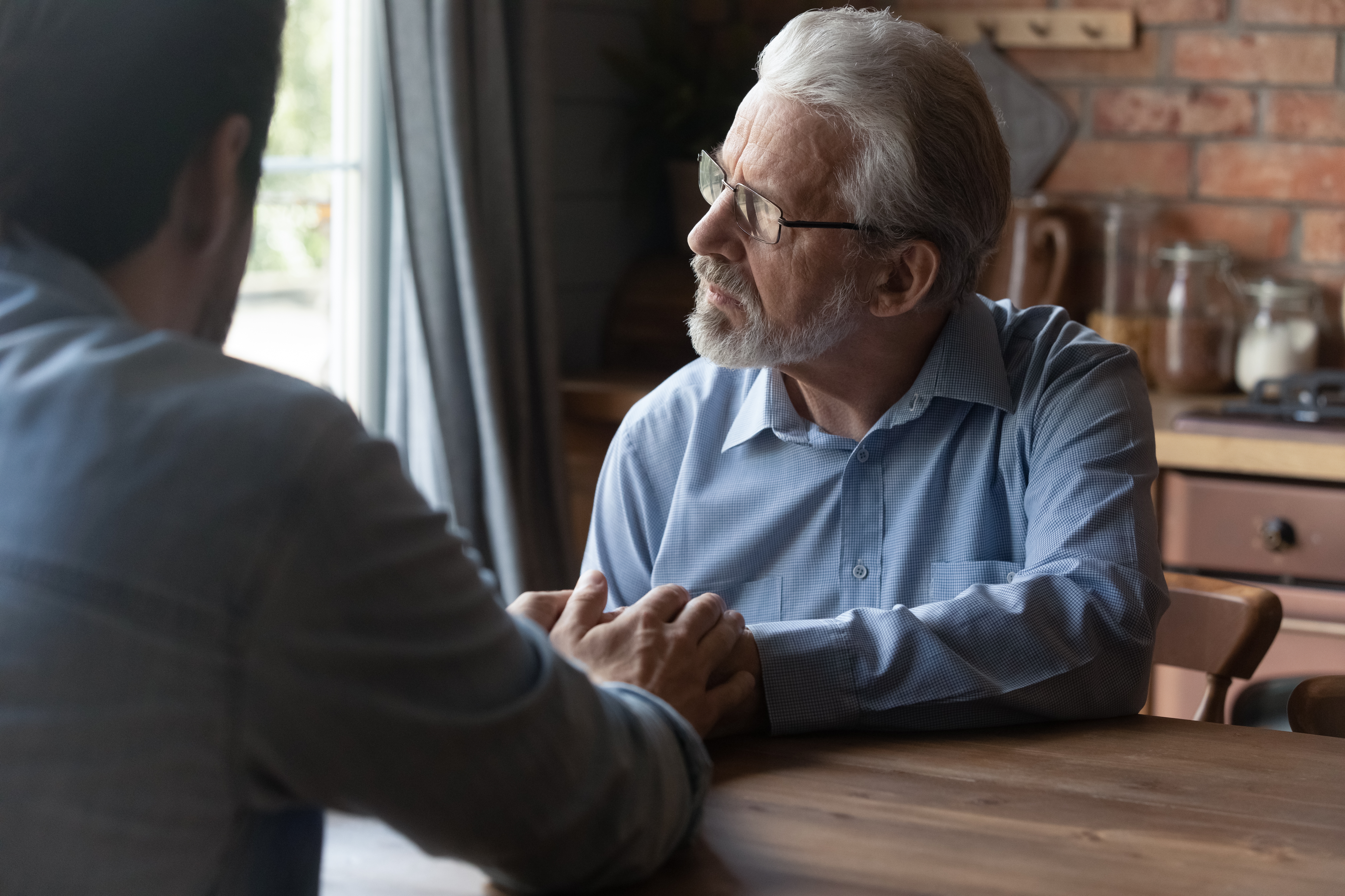 Un joven consuela a un hombre mayor que mira hacia otro lado | Foto: Shutterstock