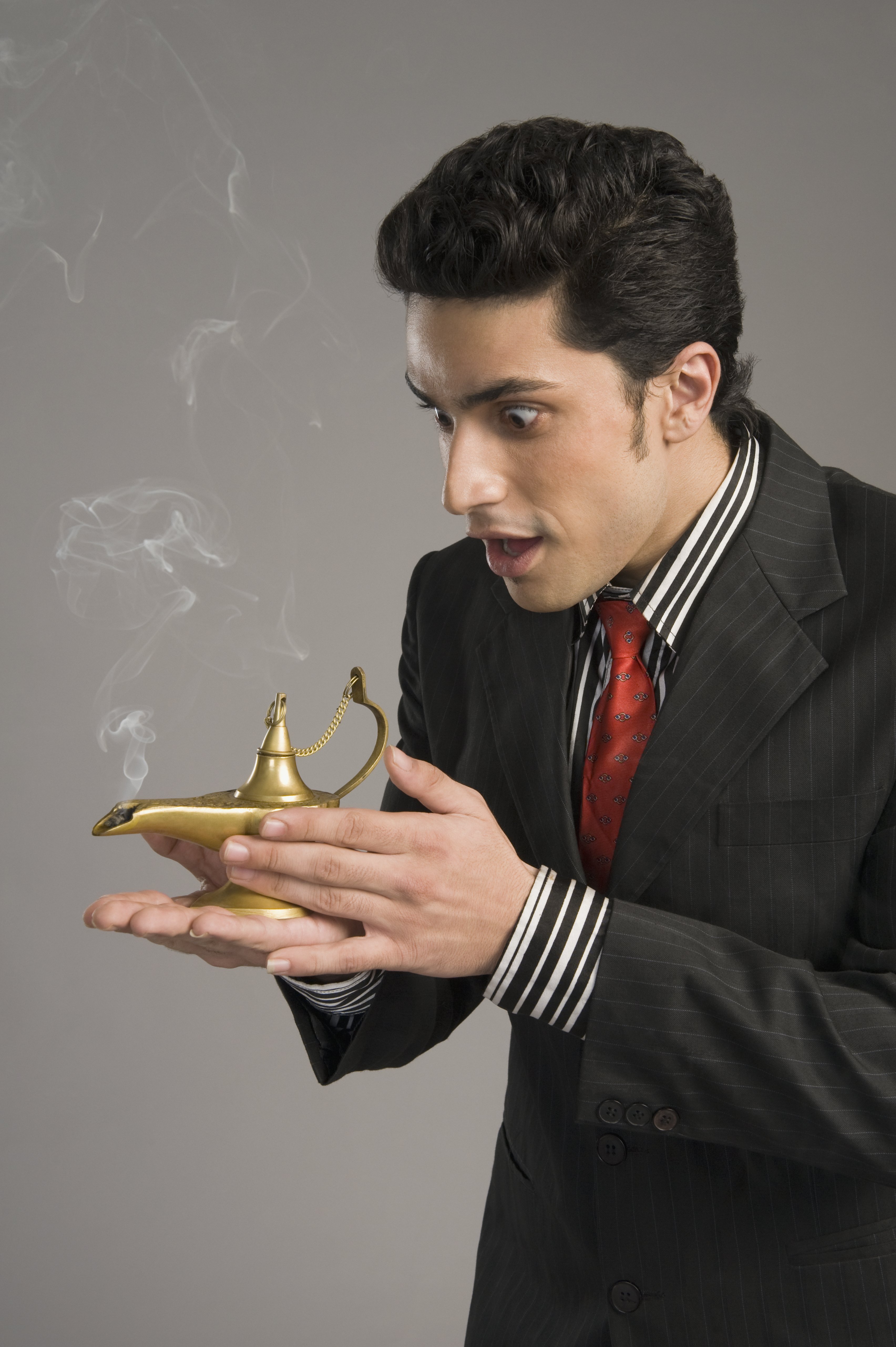 Hombre con expresión de sorpresa en su rostro, frotando una lámpara “mágica” con su mano. | Foto: Shutterstock