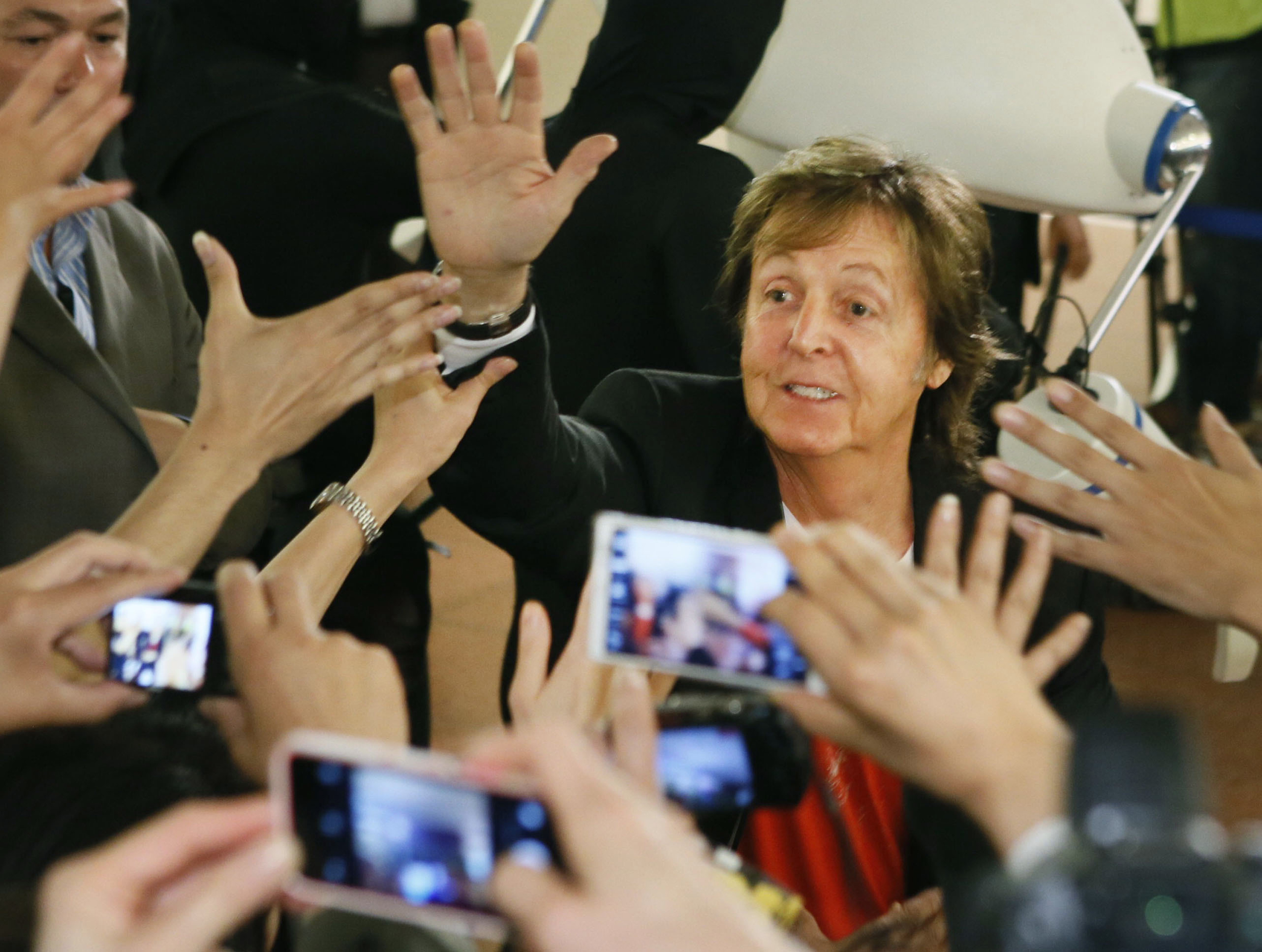 Paul McCartney choca los cinco con sus fans a su llegada al aeropuerto Haneda de Tokio, para dar un concierto en Japón, el 15 de mayo de 2014. | Fuente: Getty Images
