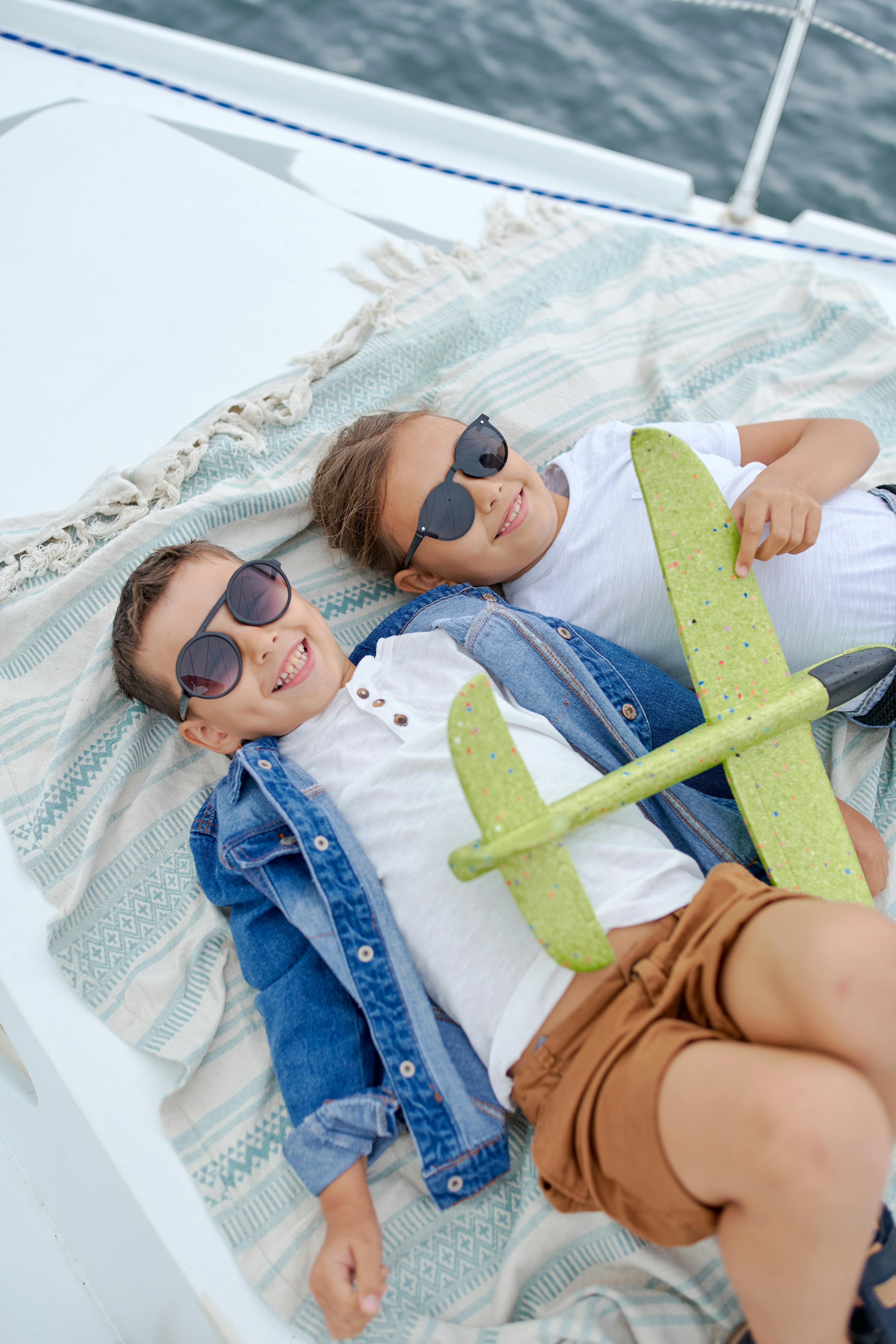 Dos niños felices tumbados boca arriba jugando con un avión | Foto: Pexels