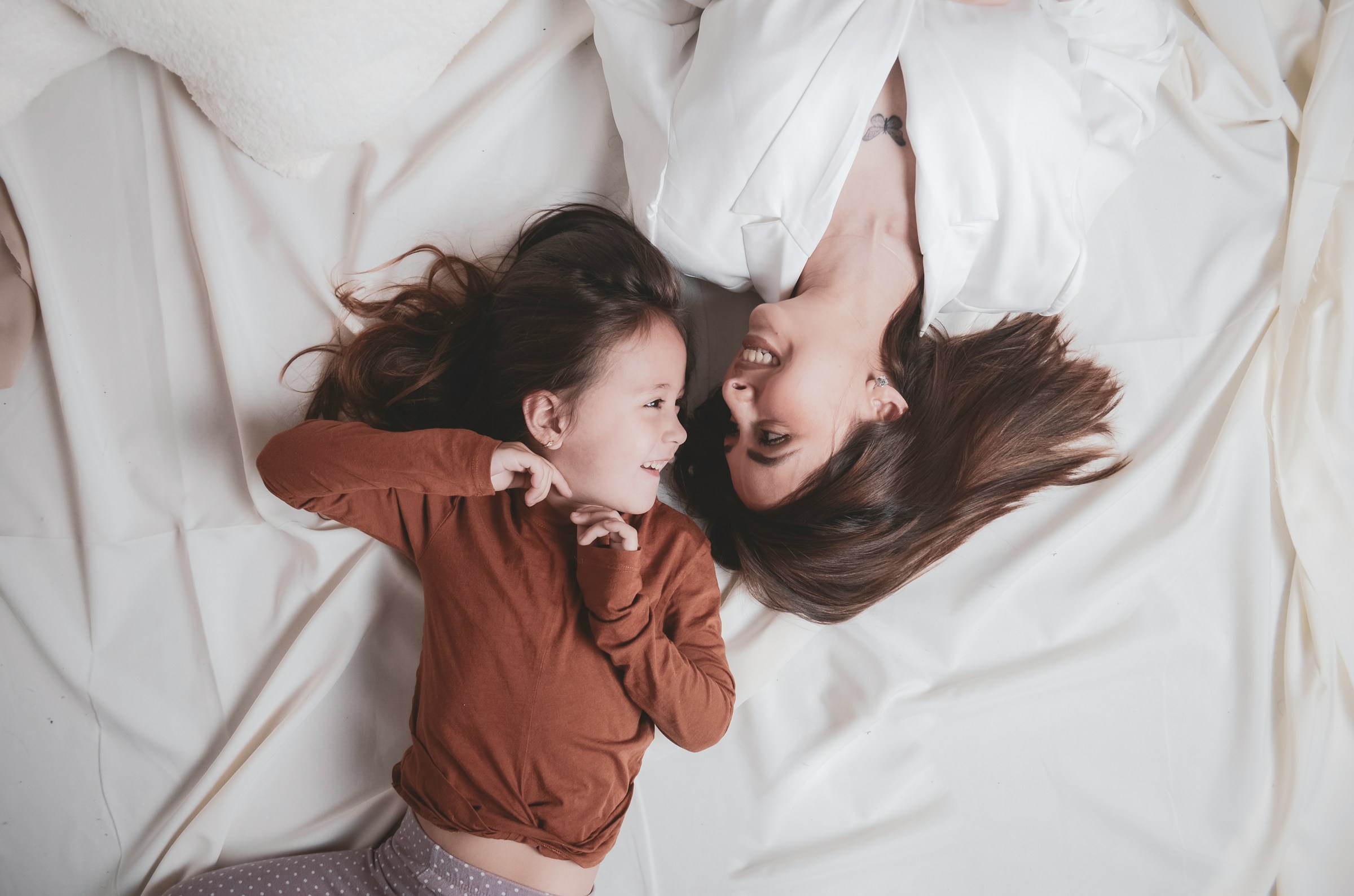 Una mujer y una niña se miran mientras están tumbadas en la cama | Fuente: Unsplash