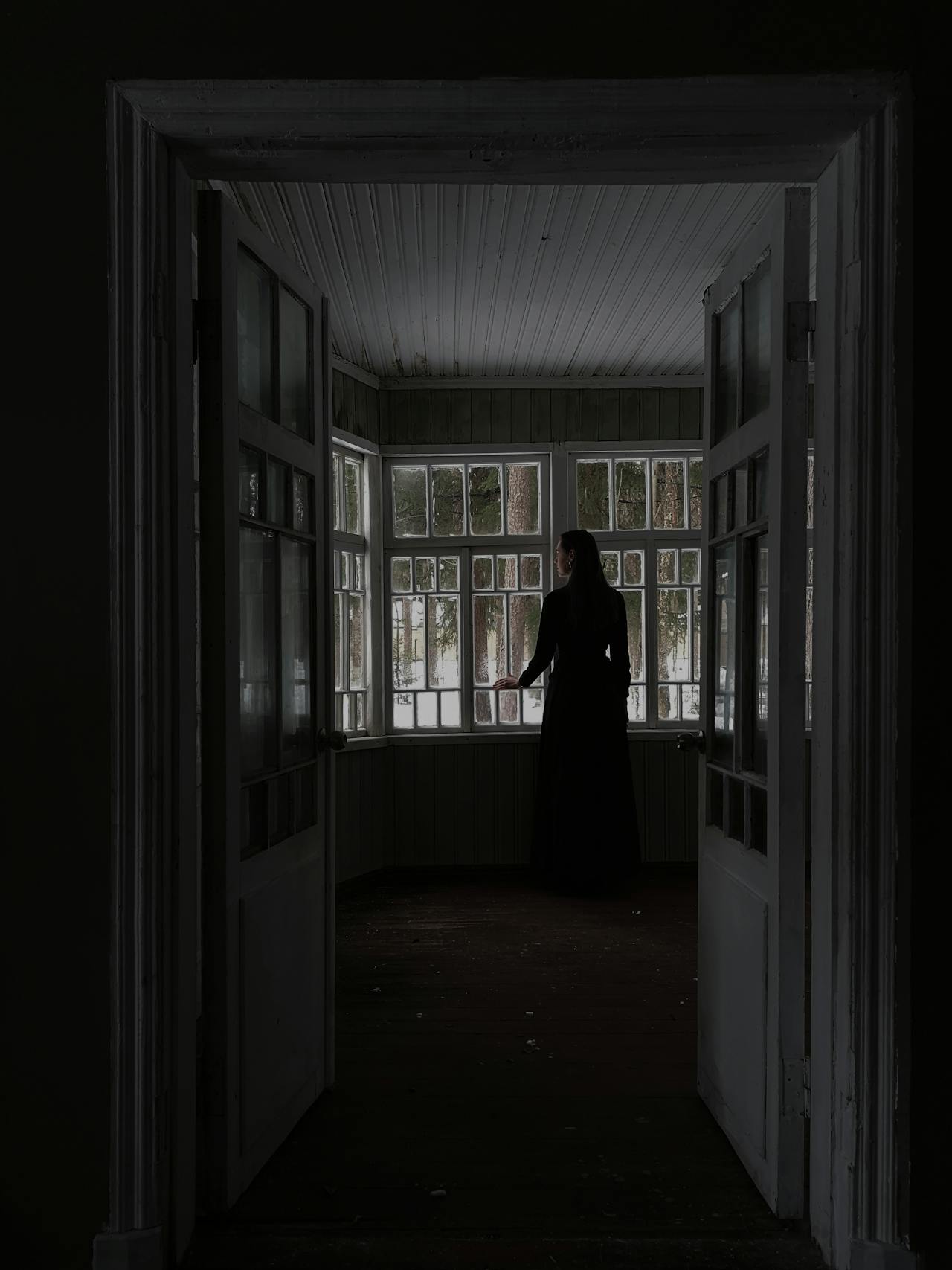 Una mujer solitaria junto a la ventana de una habitación vacía | Fuente: Pexels