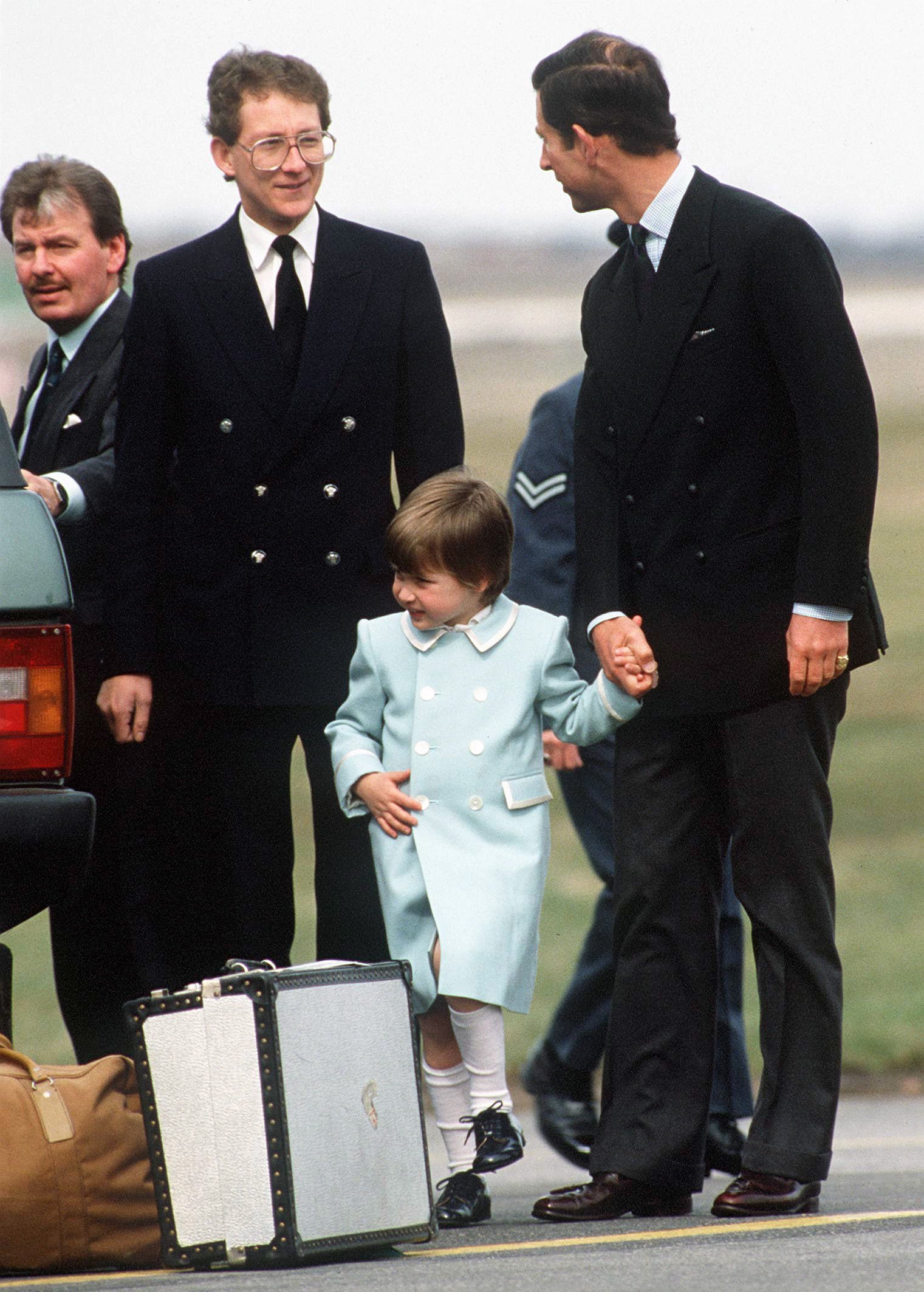El príncipe Charles y el príncipe William en el aeropuerto de Aberdeen con Ken Stronach, el ayuda de cámara real (junto al coche, con bigote) y el chófer Tim Williams, el 13 de abril de 1987. | Foto: Getty Images