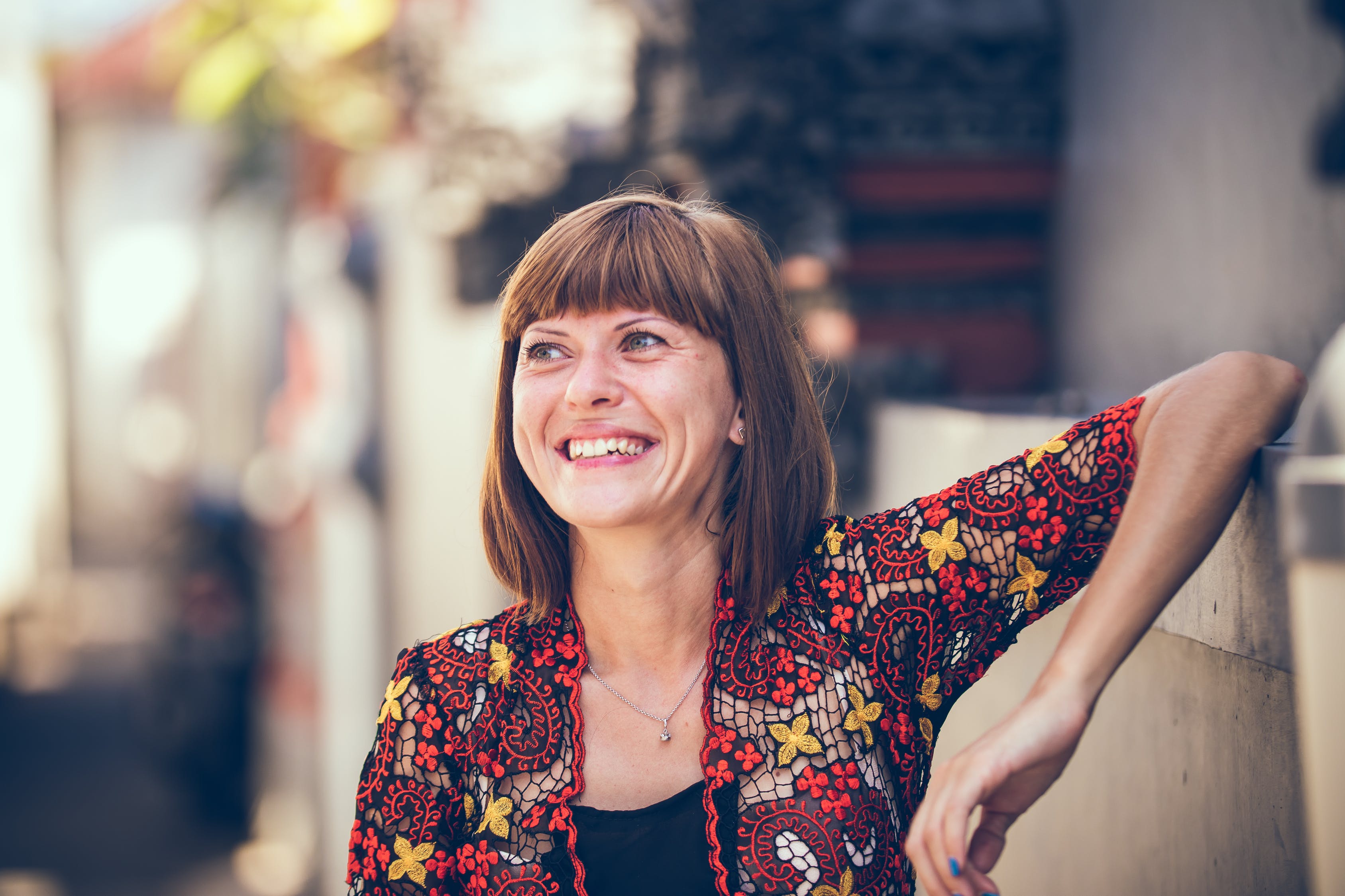 Mujer sonriendo recostada de un muro. | Foto: Pexels