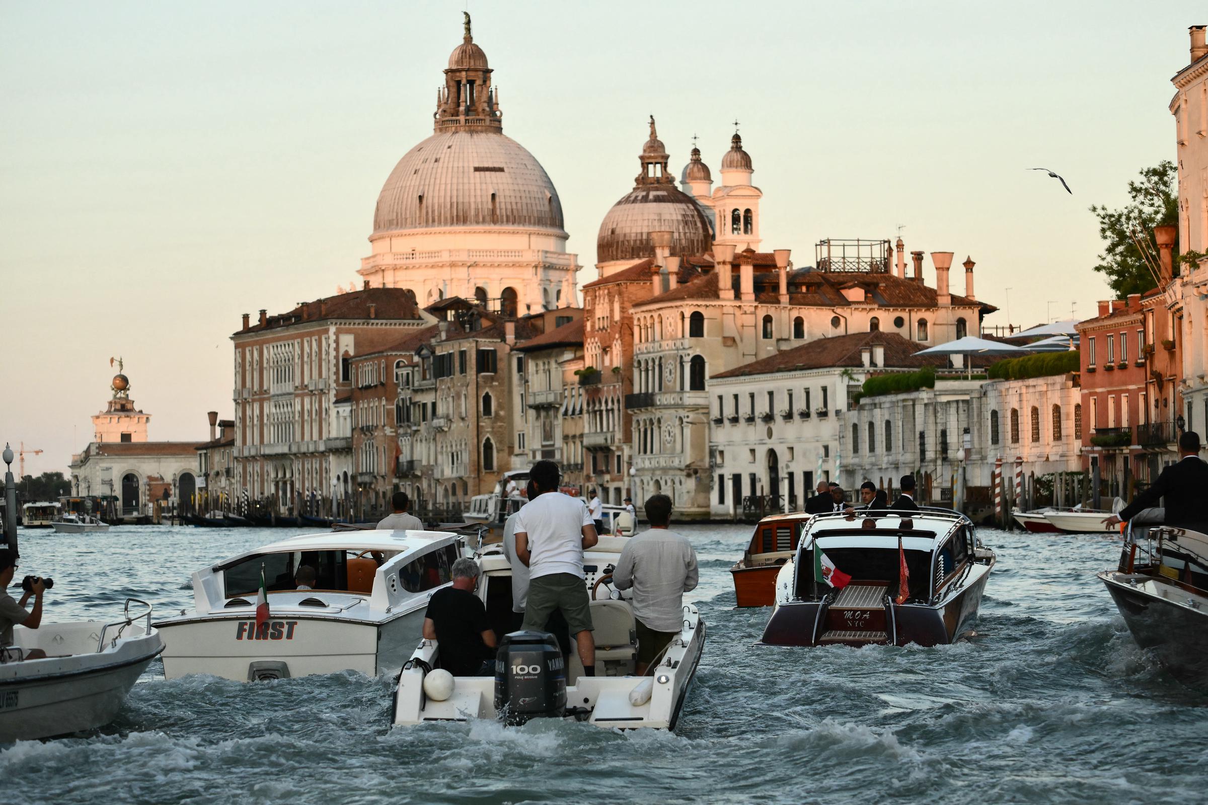 Las lanchas motoras zigzaguean por el canal mientras la luz dorada ilumina las grandes cúpulas y fachadas históricas de Venecia, captando la animada escena que sigue al taxi acuático de Jeff Bezos y Lauren Sánchez.
