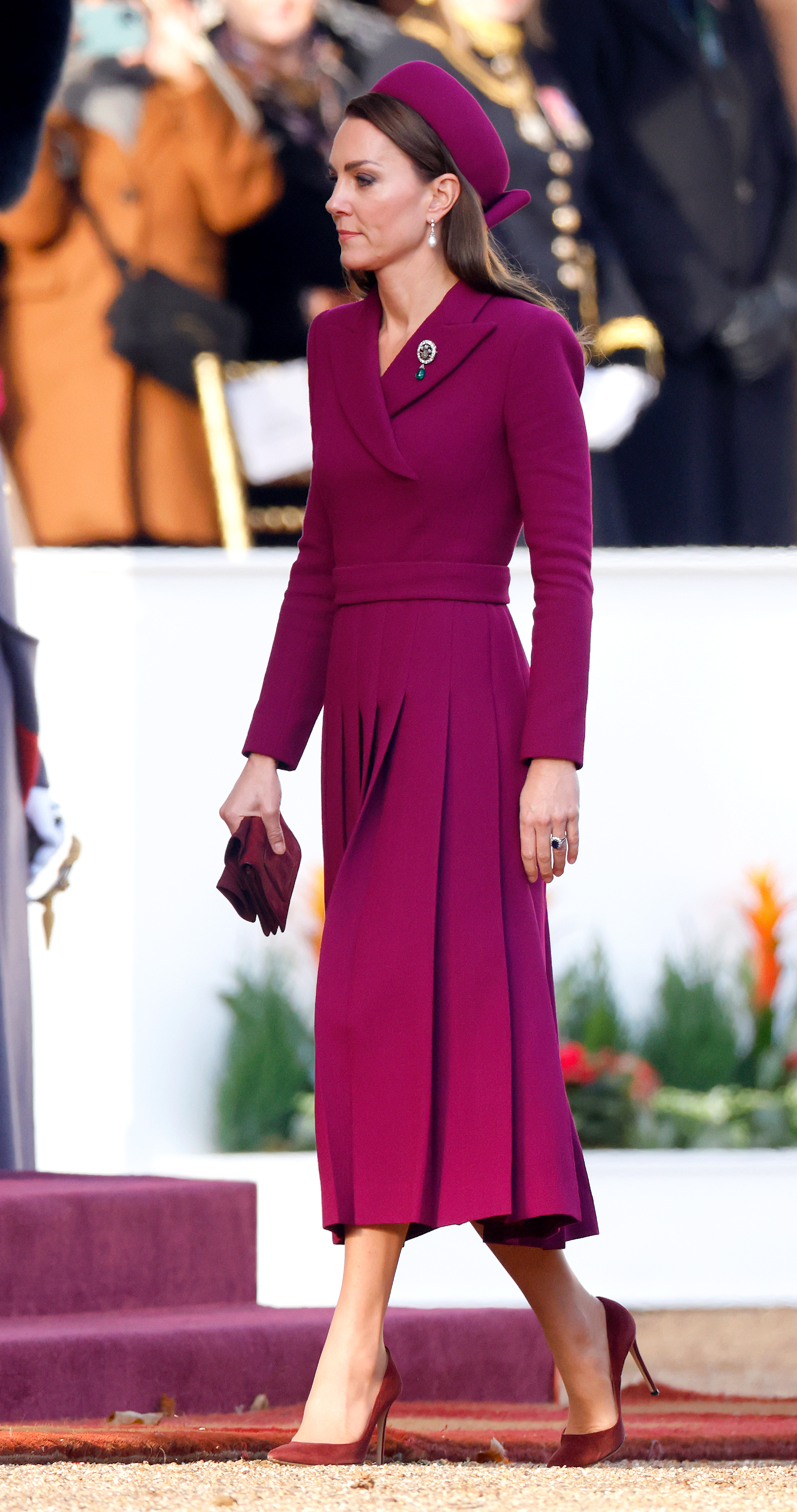 Catherine, princesa de Gales, llega a Horse Guards Parade, Londres, el 22 de noviembre de 2022, para la bienvenida al presidente sudafricano Cyril Ramaphosa, durante la primera visita de Estado bajo el reinado de Charles III. Luce un conjunto magenta con vestido-abrigo entallado de Emilia Wickstead, cuello asimétrico, cinturón y falda plisada, sombrero tipo pastillero de Sean Barrett, zapatos y guantes de gamuza burdeos, pendientes de perlas de la princesa Diana y el broche de las tres plumas de la reina Alexandra en la solapa. | Fuente: Getty Images