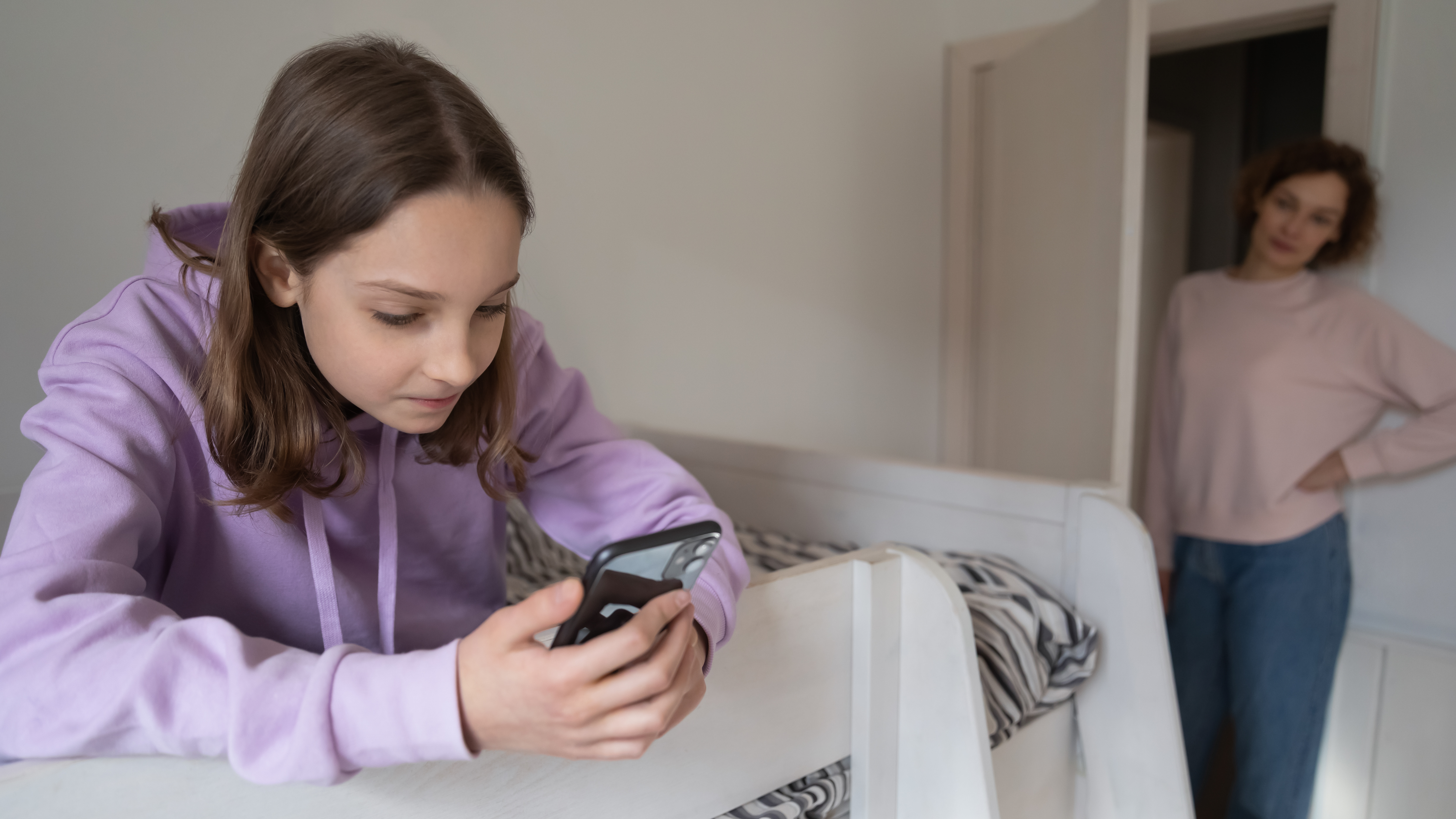 Una chica utilizando un teléfono mientras una mujer la observa | Fuente: Shutterstock
