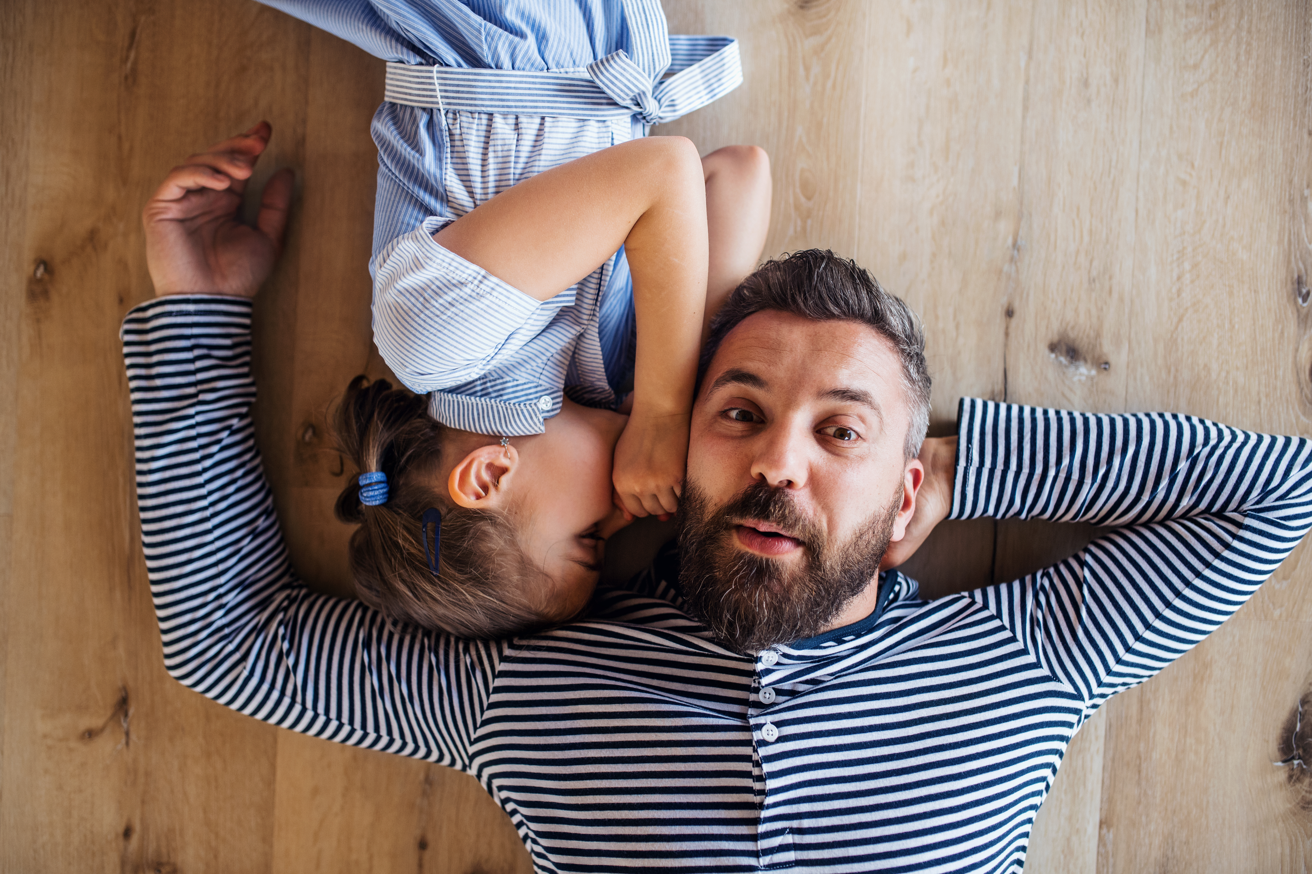 Vista superior de un padre maduro y una hija pequeña tumbados en el suelo en casa, susurrando | Foto: Getty Images