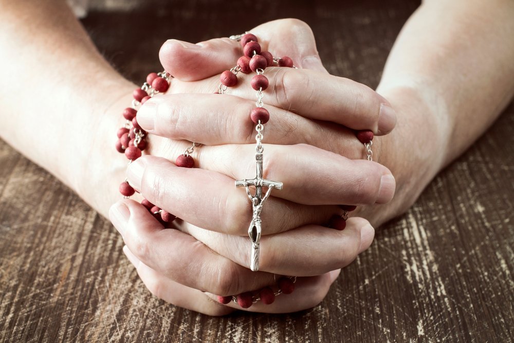 Persona rezando con un rosario en sus manos.| Fuente: Shutterstock