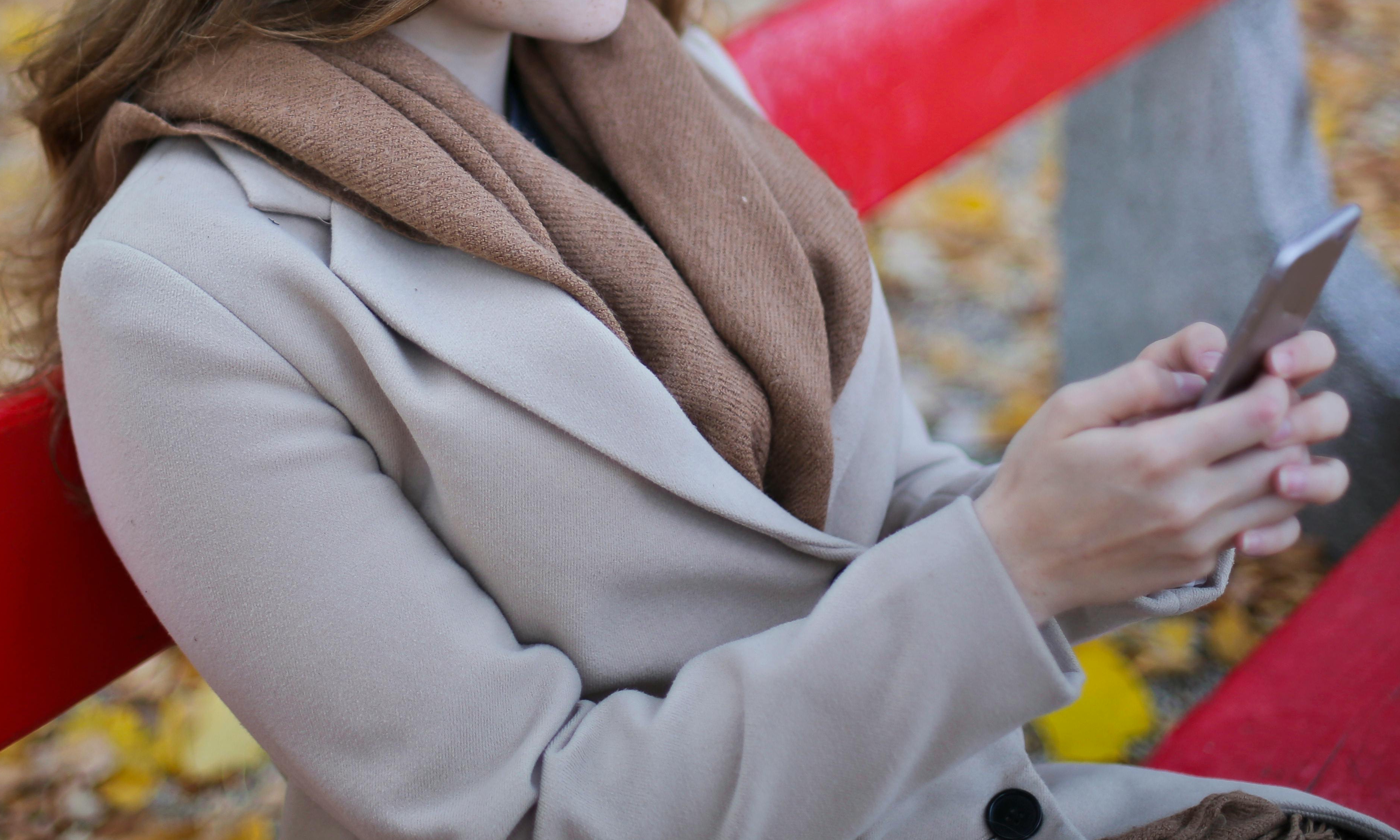 Una mujer sentada en un banco del parque con un móvil en las manos | Fuente: Pexels