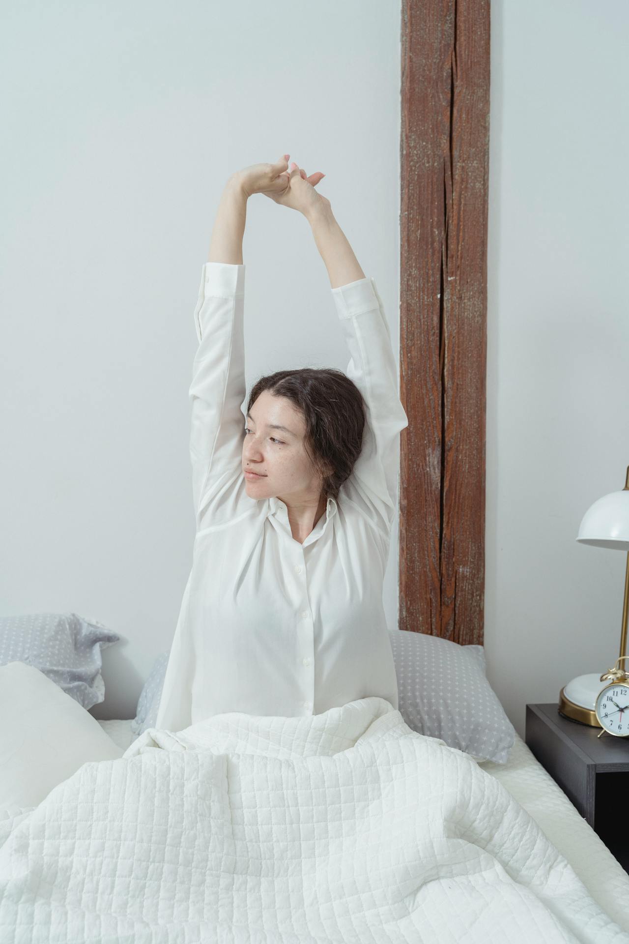 Una donna che si stira le braccia mentre è seduta sul letto | Fonte: Pexels
