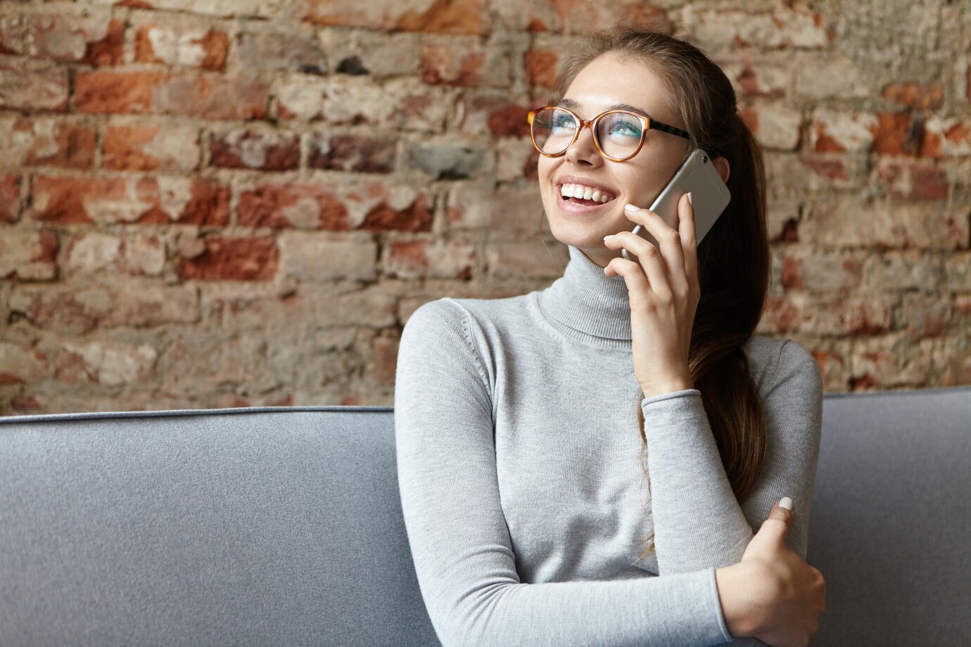 Una mujer sonriente hablando por teléfono mirando hacia arriba ⏐ Fuente: Freepik