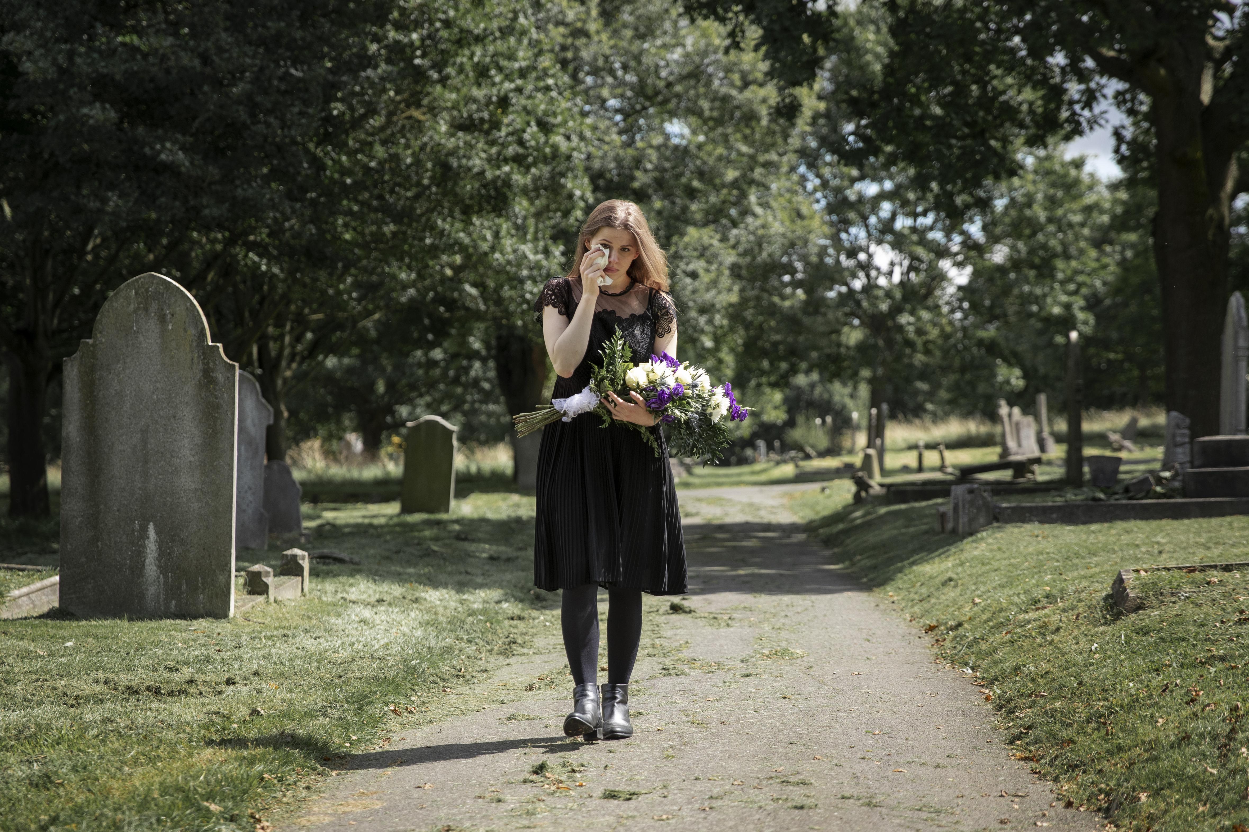 Una mujer afligida sostiene un ramo de flores en un cementerio | Fuente: Freepik