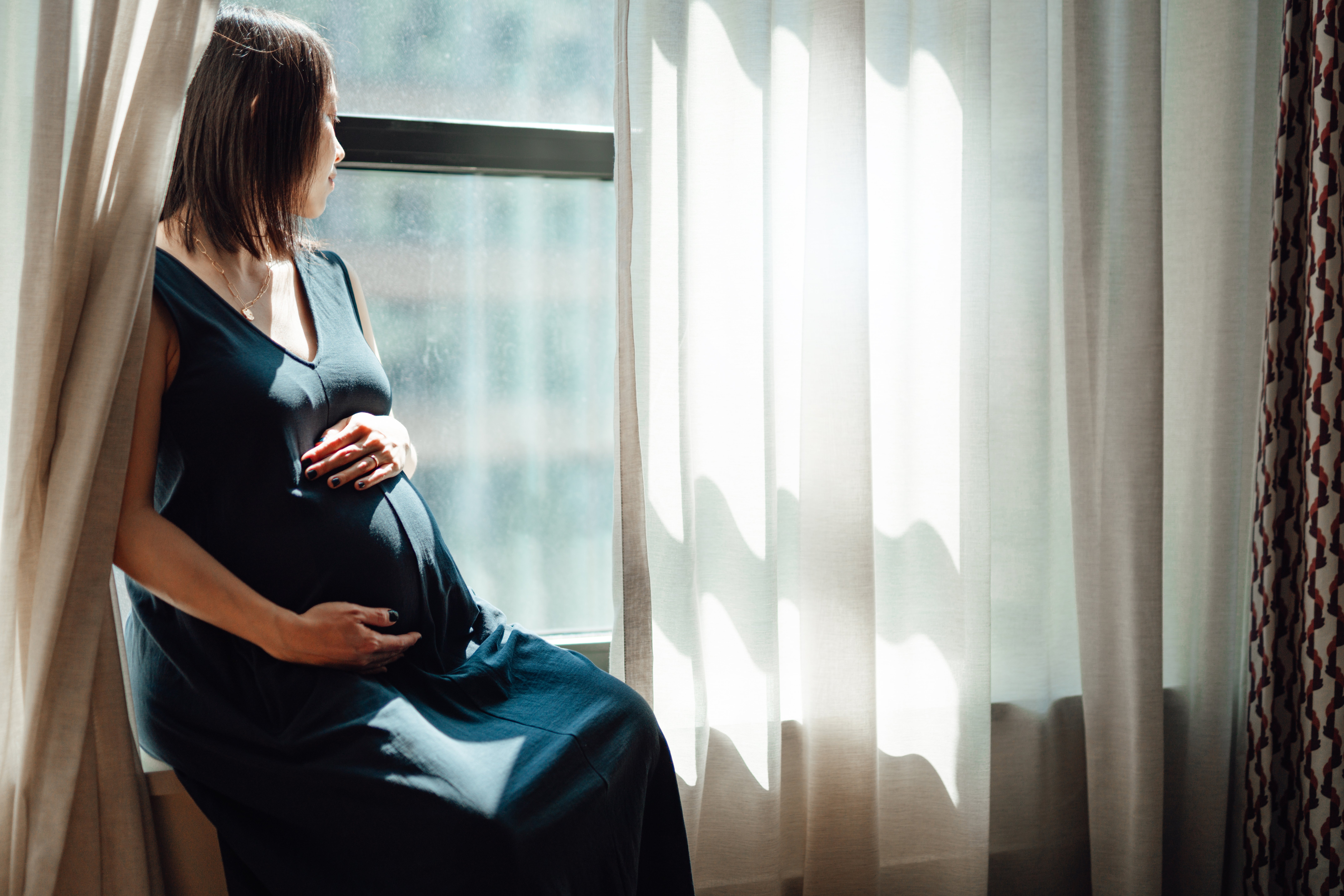 Una mujer embarazada sentada en una ventana mirando hacia afuera. | Foto: Getty Images