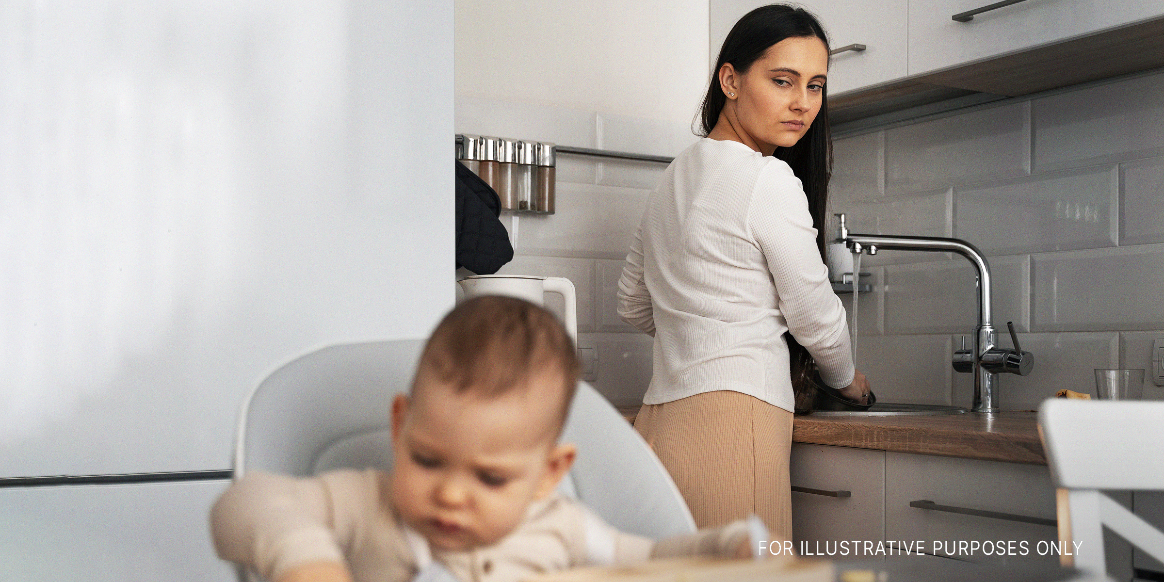 Una mujer lavando los platos y mirando a un bebé | Foto: Freepik