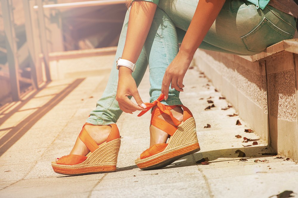 Mujer amarrándose sus sandalias naranjas. | Foto: Shutterstock
