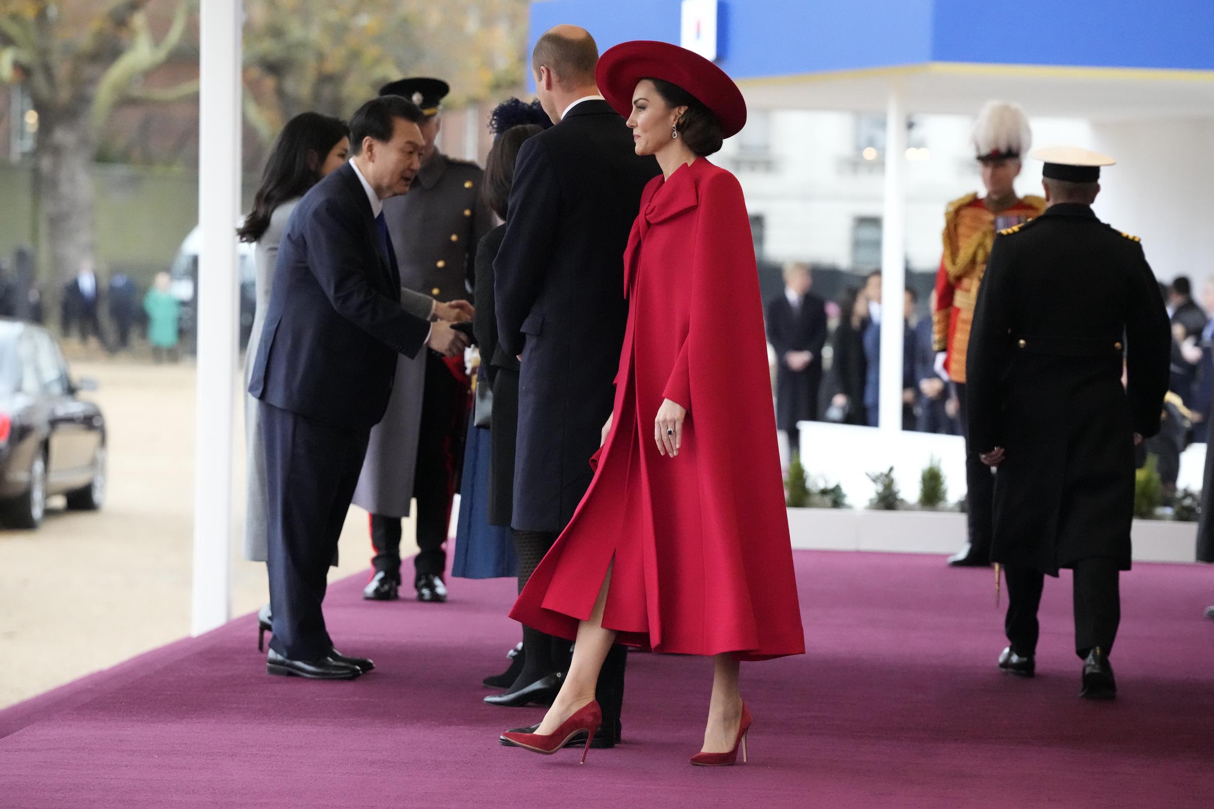 Catherine, princesa de Gales, hace una entrada impactante a la tribuna de Horse Guards Parade, Londres, el 21 de noviembre de 2023, durante la bienvenida ceremonial por la visita de Estado de Corea del Sur. Luce un conjunto rojo escarlata con abrigo de capa a medida de Catherine Walker, un gran lazo y vestido a juego, sombrero de ala ancha de Sarah Cant, pendientes de zafiros y diamantes de la princesa Diana y zapatos de gamuza roja de Gianvito Rossi. | Fuente: Getty Images