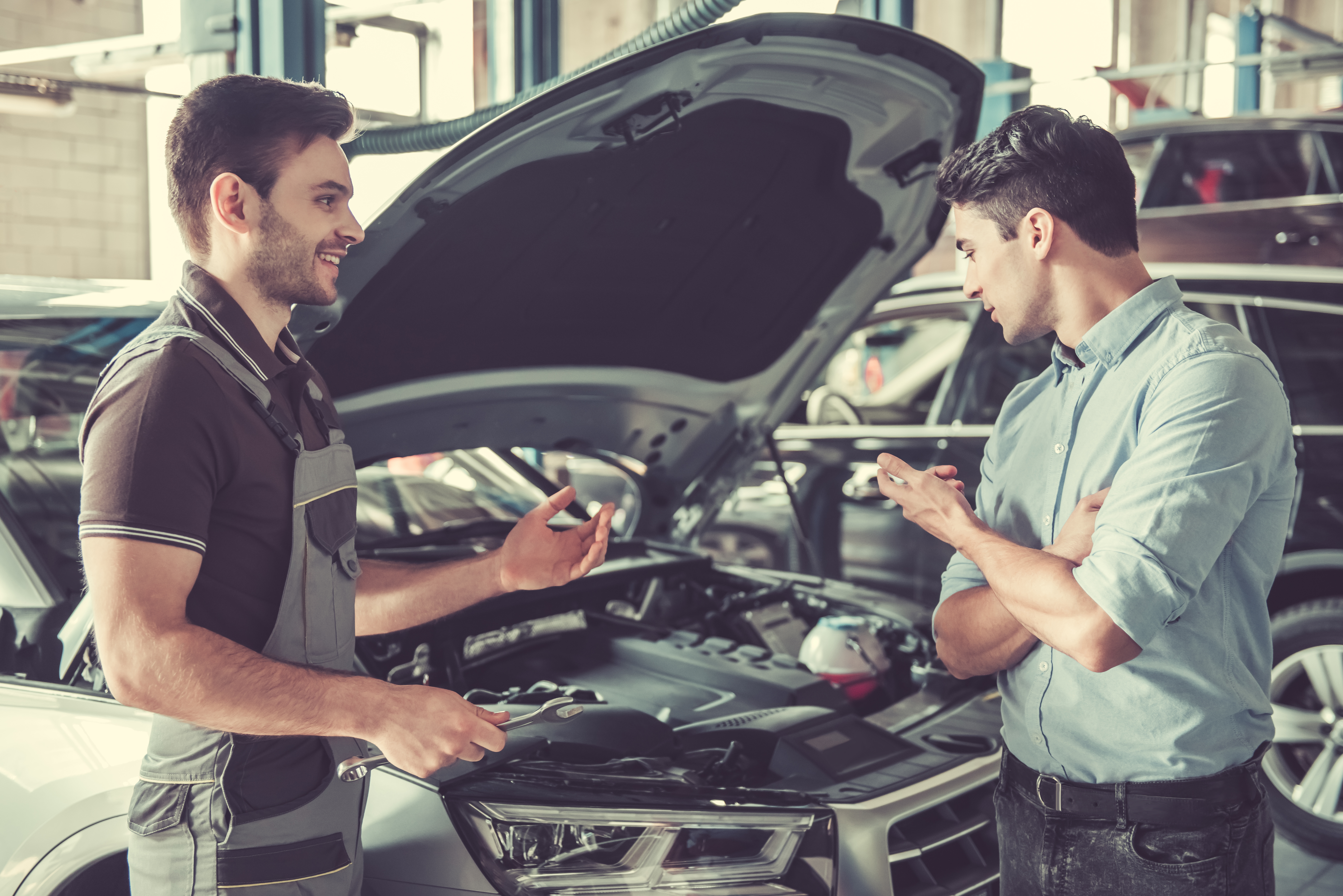 En el taller mecánico. Un joven y guapo mecánico de coches con uniforme habla con un cliente y sonríe. | Fuente: Shutterstock