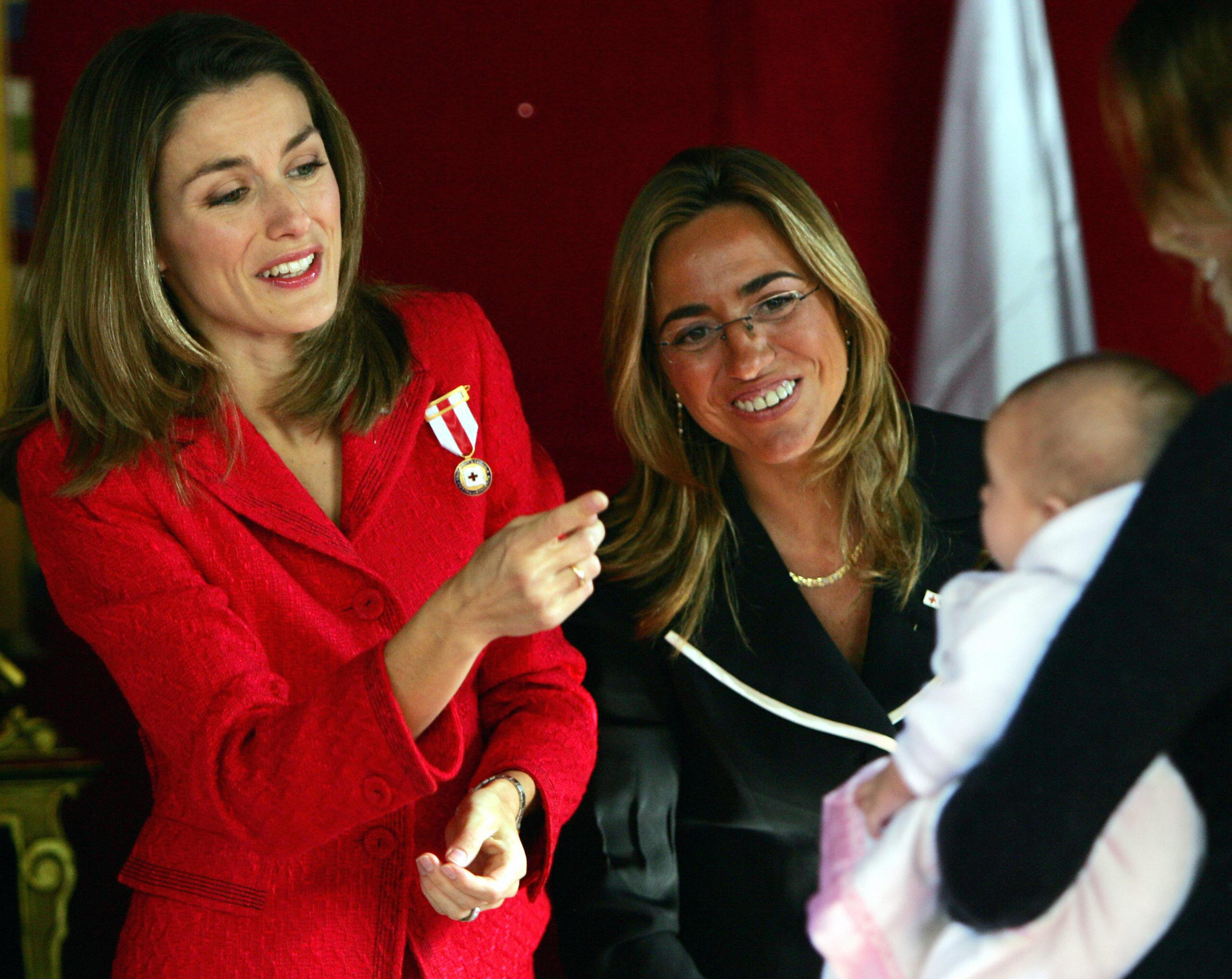 Letizia (I) mira a un bebé junto a la vicepresidenta del Congreso, Carmen Chacón (D), durante el "Día de la Banderita de la Cruz Roja" en Madrid, el 26 de octubre de 2004. | Fuente: Getty Images