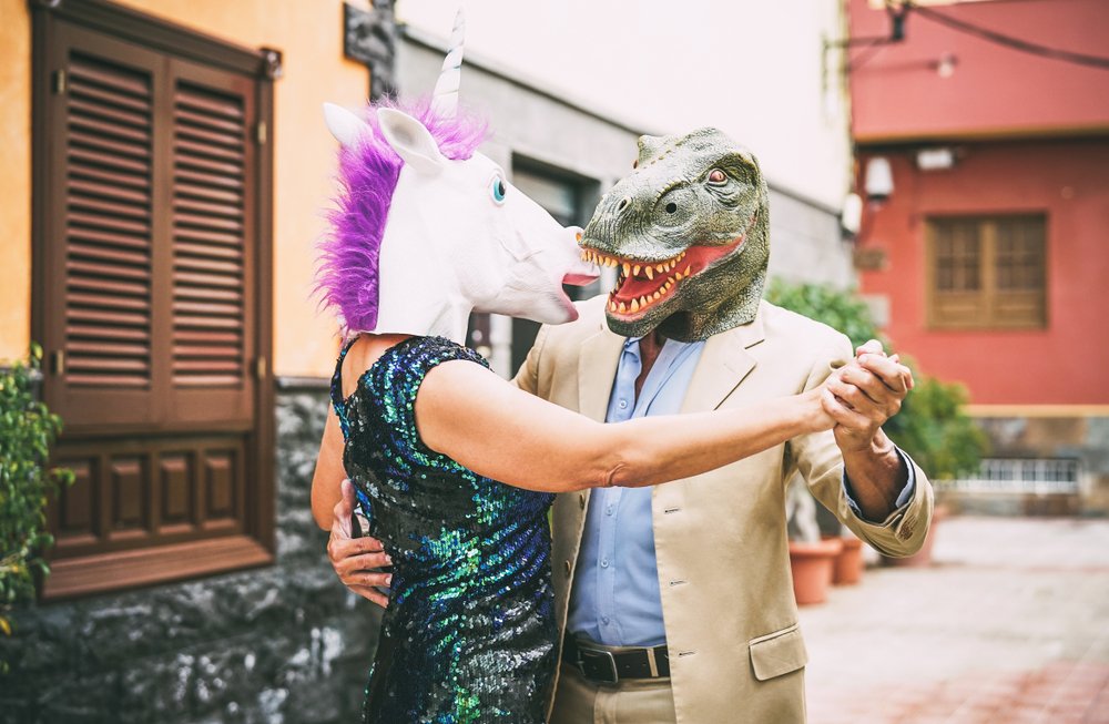 Pareja excéntrica bailando con máscaras de unicornio y de dinosaurio. | Foto: Shutterstock