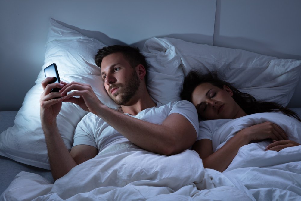 Hombre enviando mensajes de texto a altas horas de la noche mientras su novia duerme. | Foto: Shutterstock