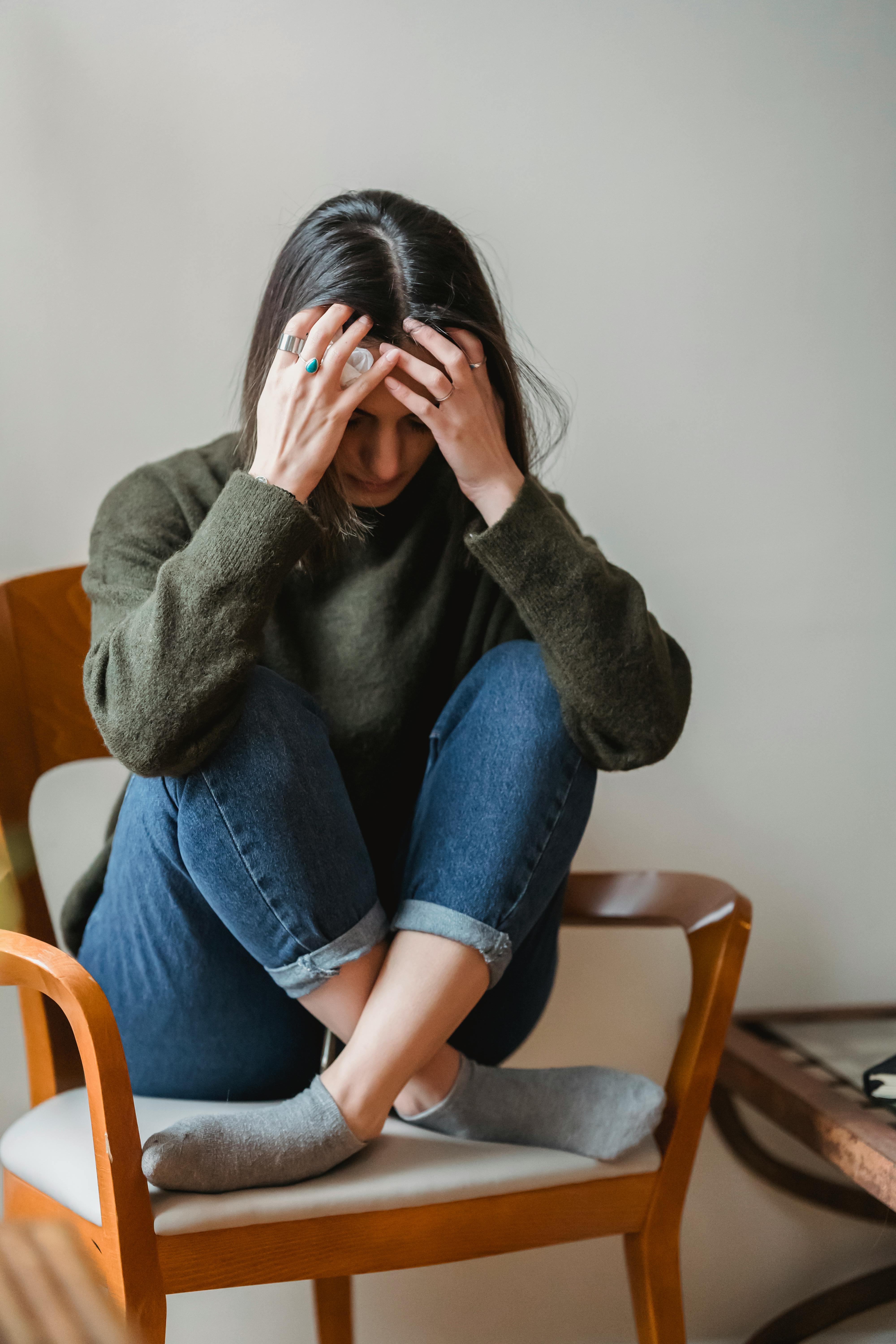 Una mujer angustiada sentada con las piernas cruzadas en una silla | Fuente: Pexels