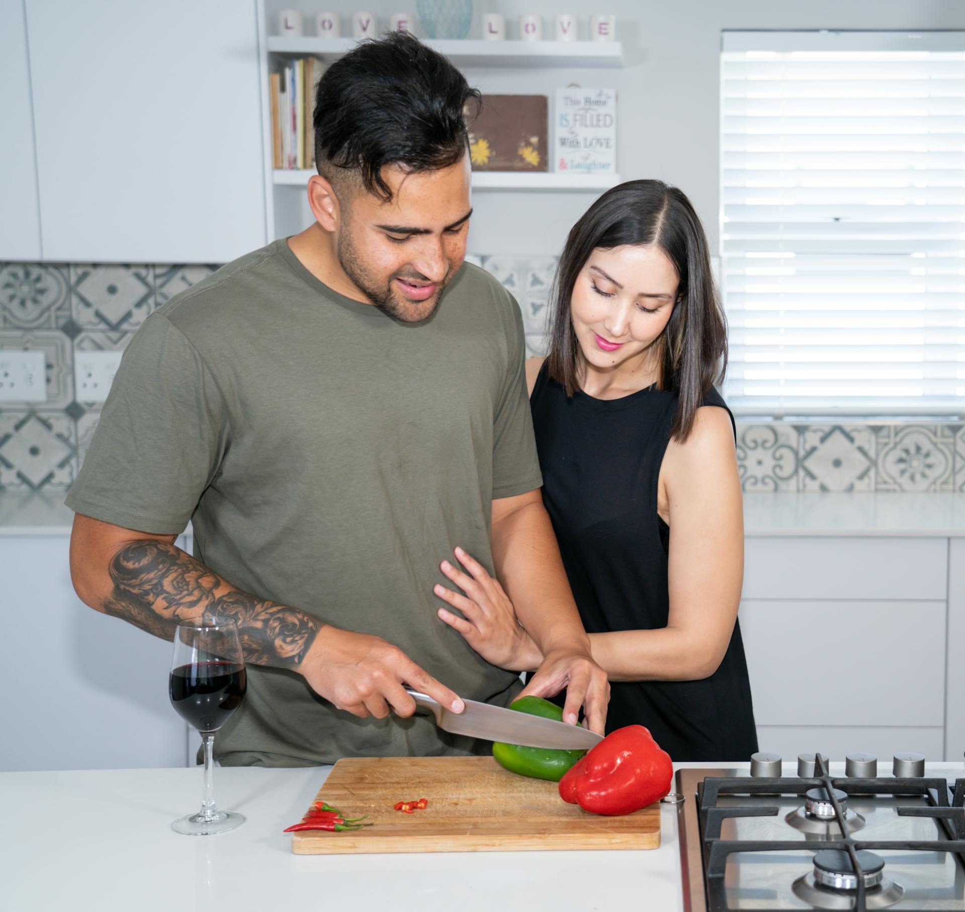 Una mujer observa cómo su marido corta verduras en la cocina | Fuente: Pexels