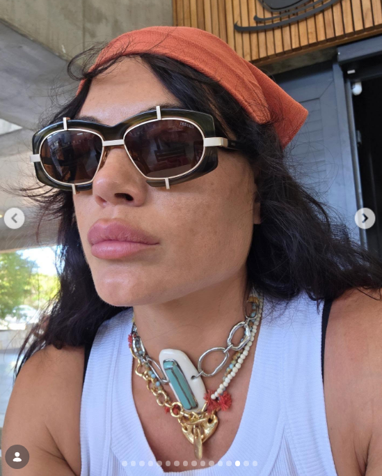 Emilia Attias lució un estilo veraniego desenfadado en un primer plano donde combinó un pañuelo color terracota sobre la cabeza con gafas de sol oscuras de armazón angular bicolor. La actriz y modelo completó su look con una camiseta básica blanca sin mangas y un llamativo conjunto de collares superpuestos de eslabones plateados, mostacillas y colgantes artesanales. | Fuente: Instagram/emilia_att