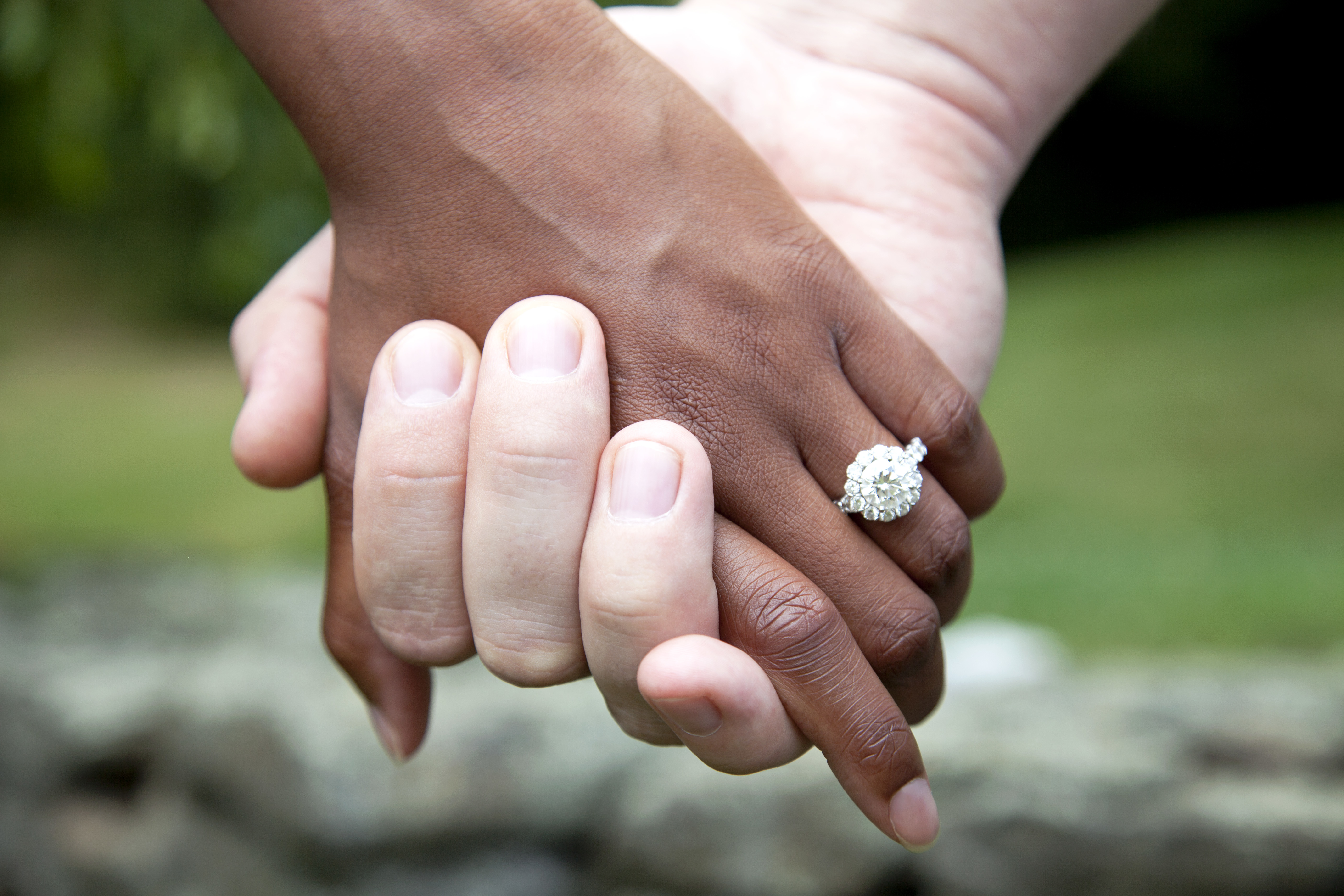 Pareja interracial de la mano, con un anillo de compromiso de diamantes | Fuente: Getty Images