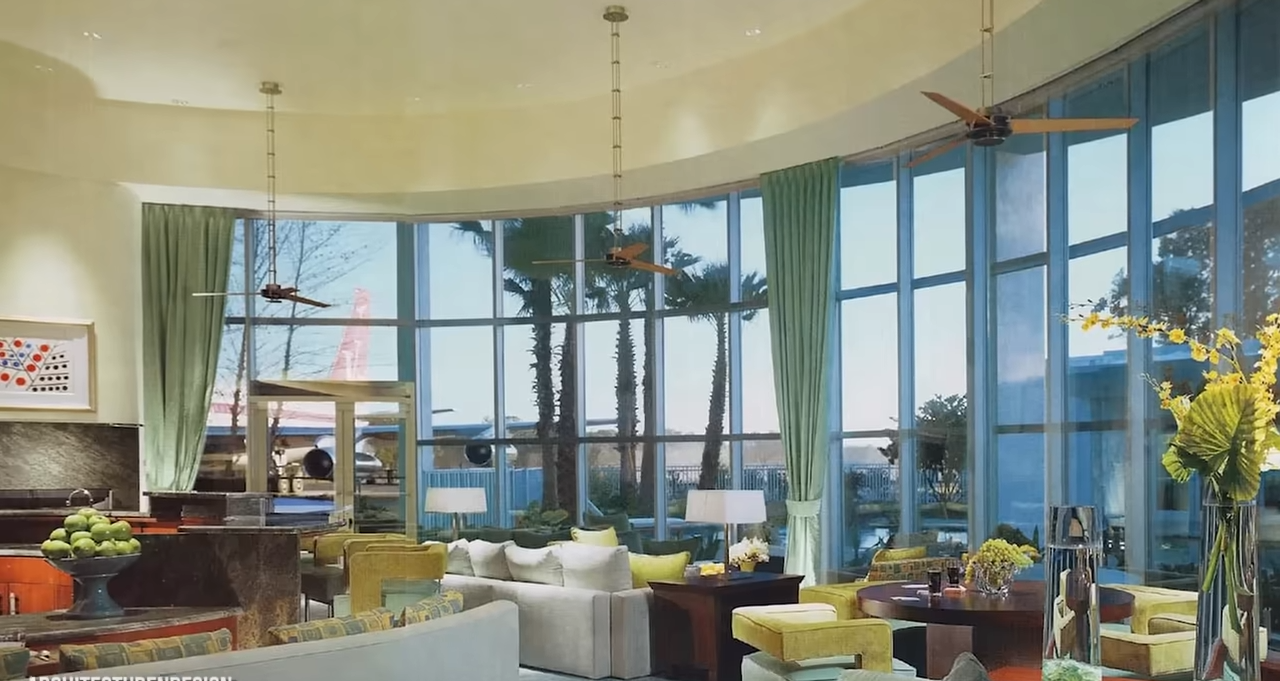 La sala de estar curva de la casa cuenta con ventanas altísimas, cortinas de color verde pálido y unas vistas inigualables de un avión que hay fuera. | Fuente: YouTube/@Therichest