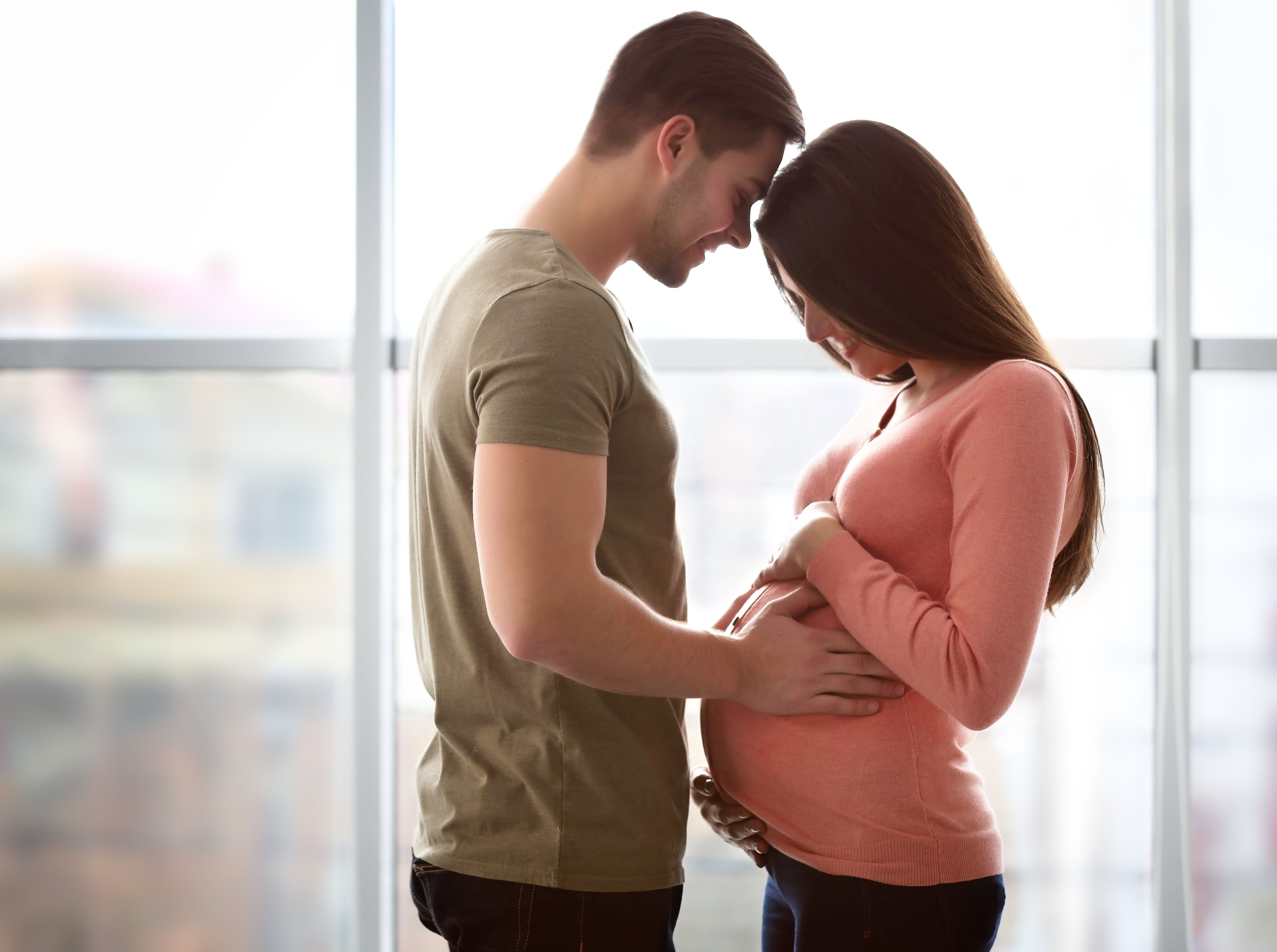 Un hombre apoya la frente en la de su mujer embarazada | Fuente: Shutterstock