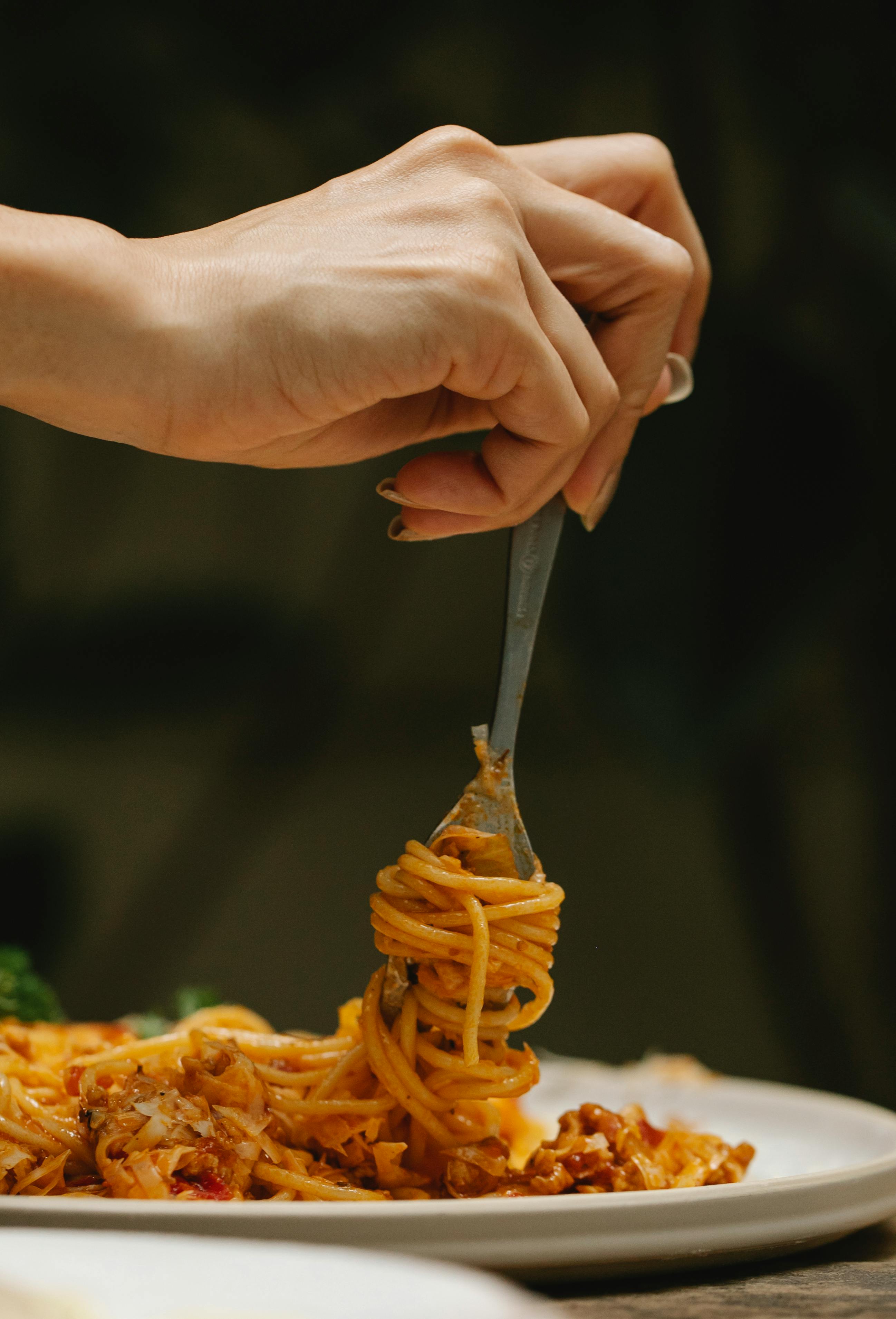Mujer enrollando espaguetis en un tenedor | Fuente: Pexels